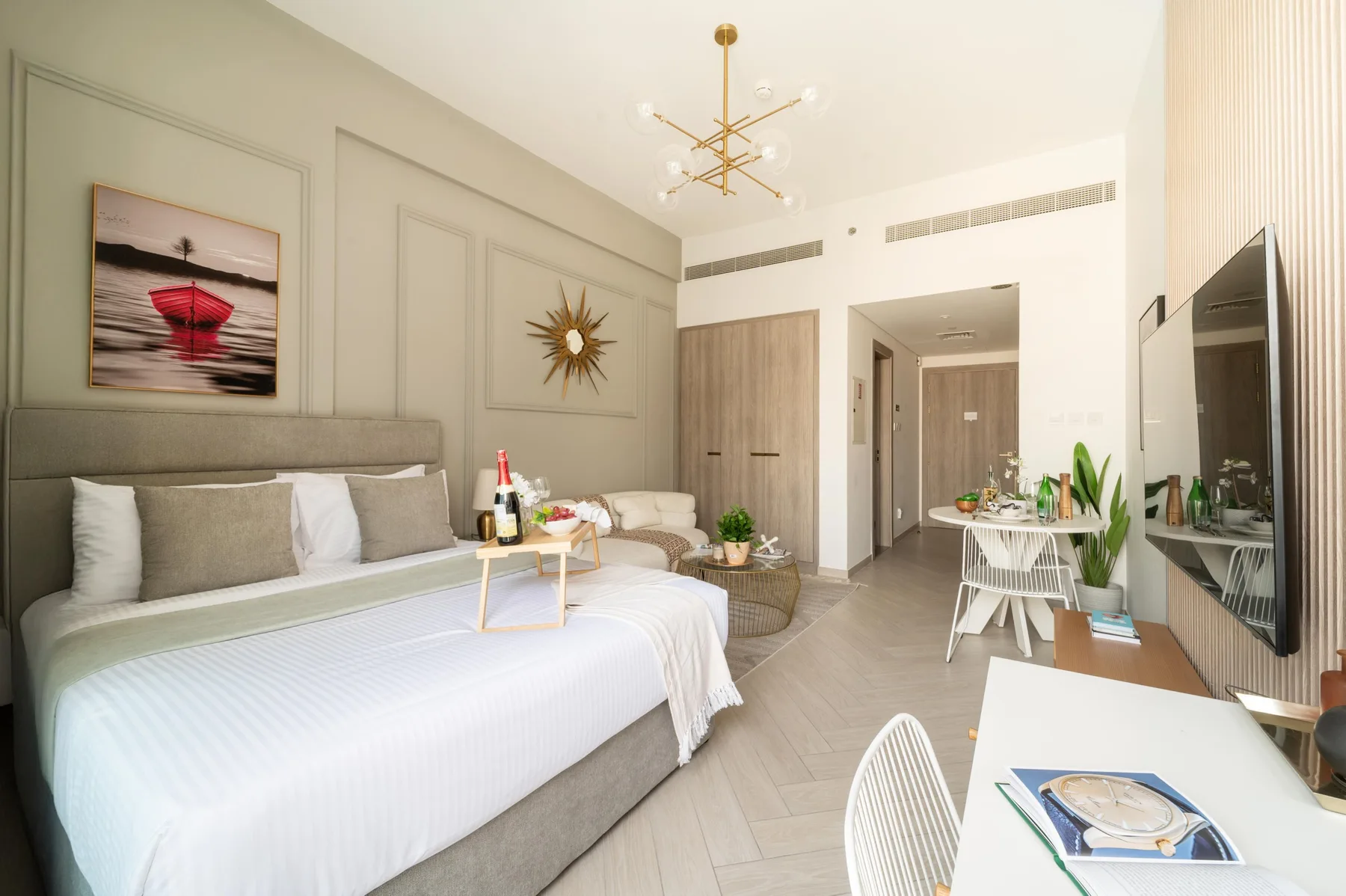 Un dormitorio luminoso con zona de comedor, cama, mesa y televisor.