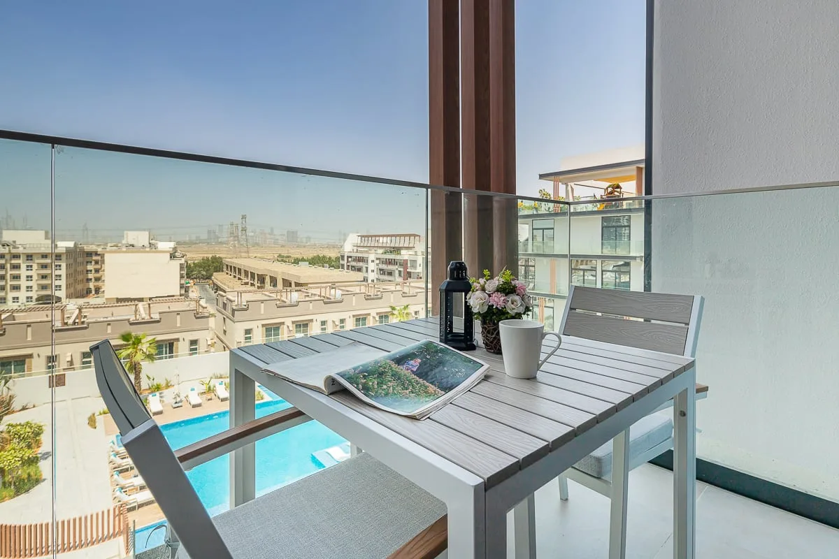 Una zona de comedor en el balcón da a una piscina y edificios cercanos.