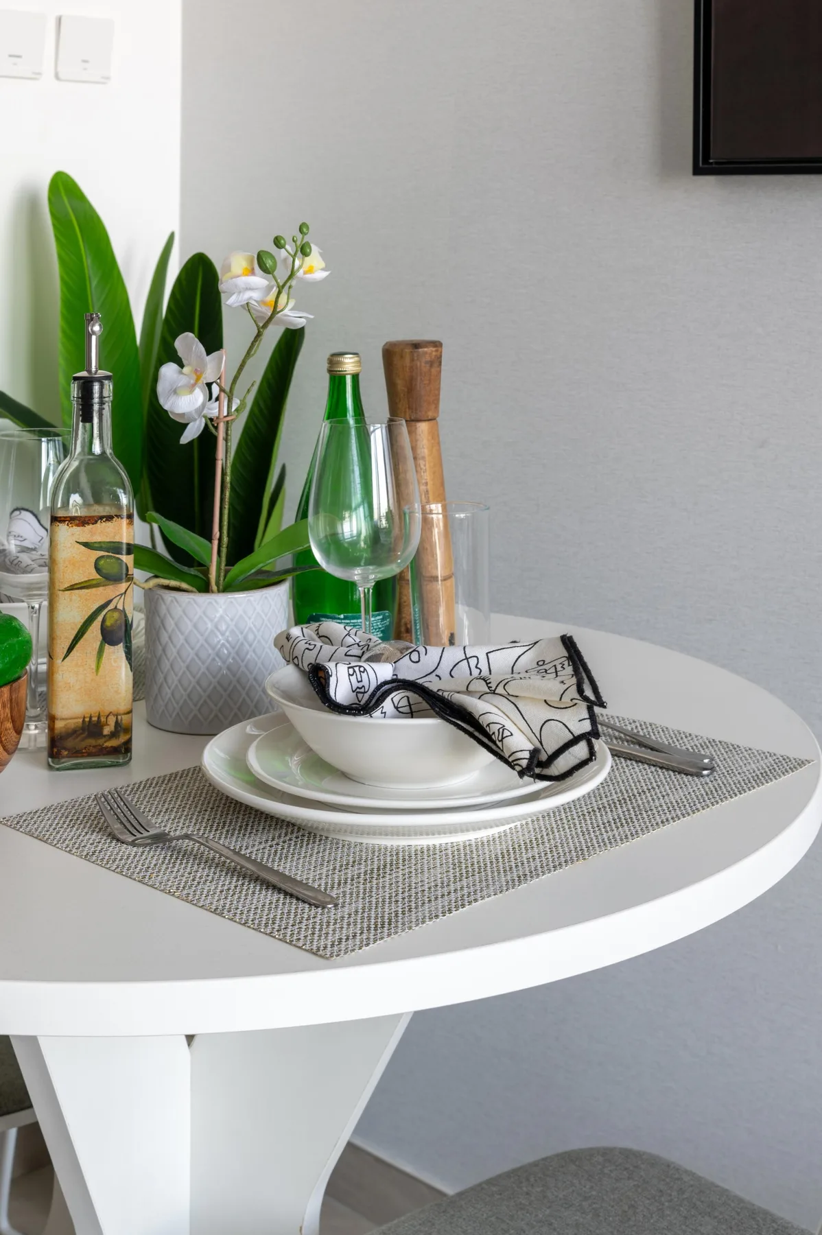 Una mesa de comedor puesta con platos, una copa y una planta con flores.