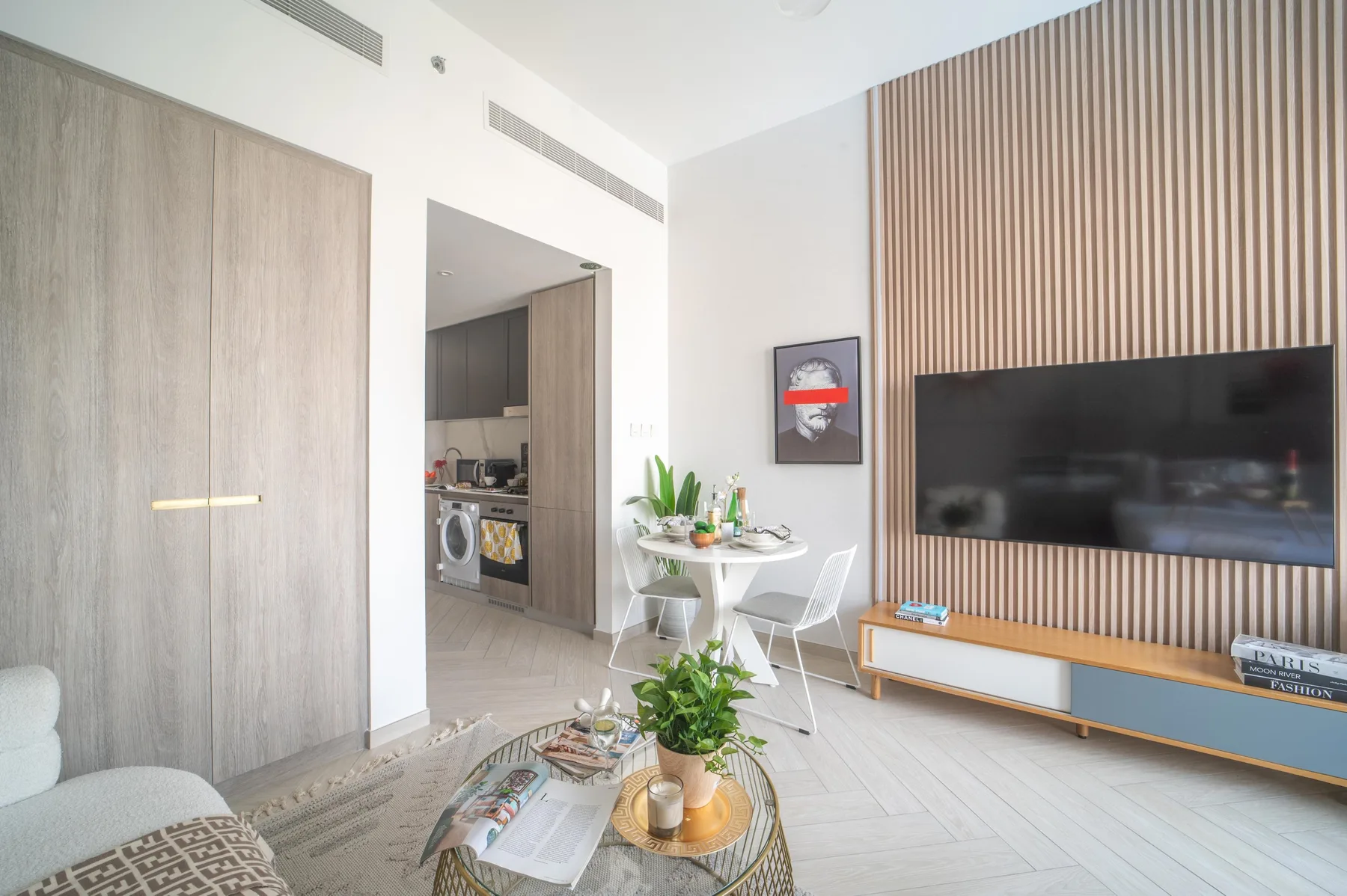 Una sala luminosa con un televisor montado en la pared y una pequeña mesa de comedor.