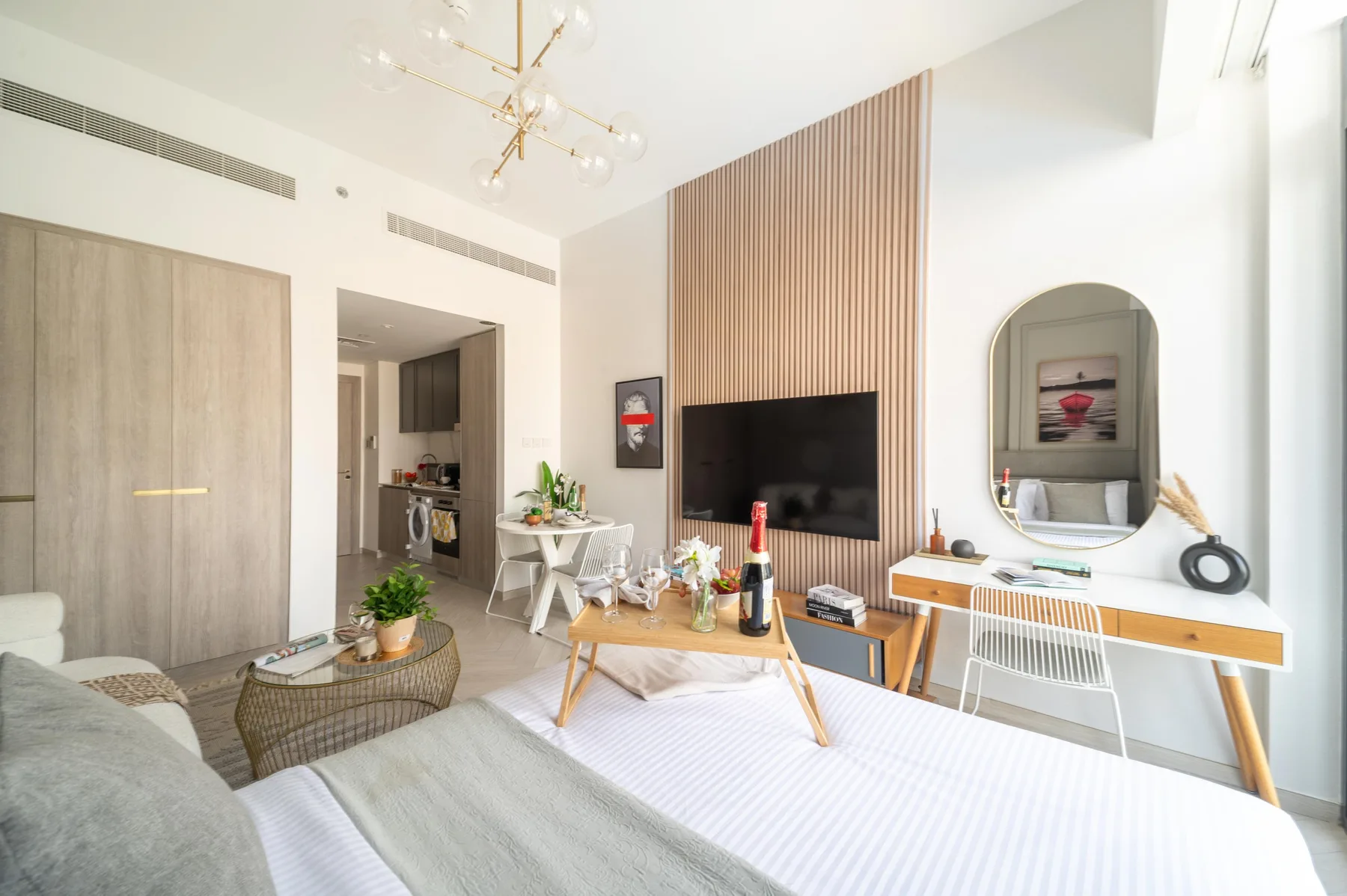 Un dormitorio luminoso con una cama frente a un televisor de pared y una pequeña zona de comedor.