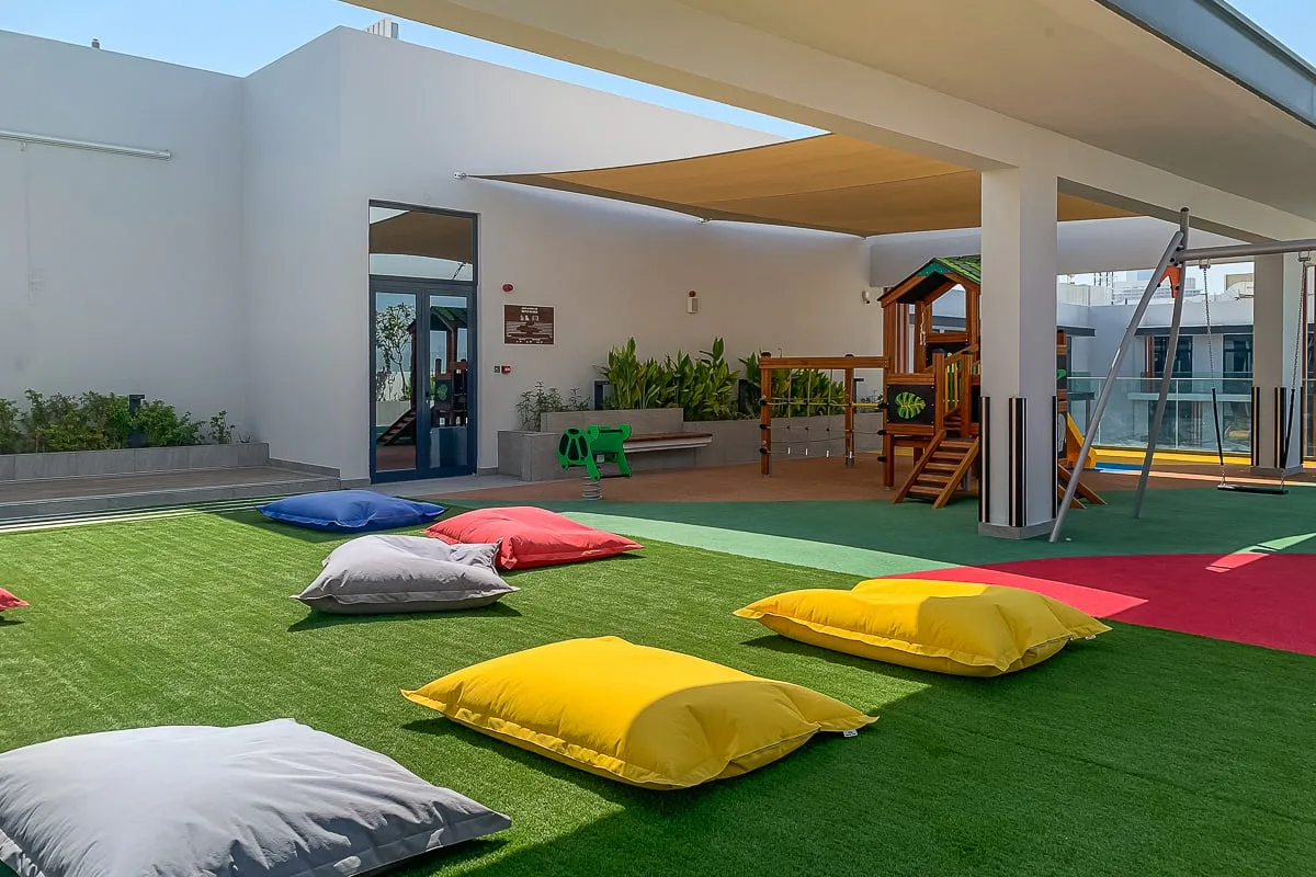 Una zona de juegos al aire libre tiene cojines de colores y una estructura de juego de madera.