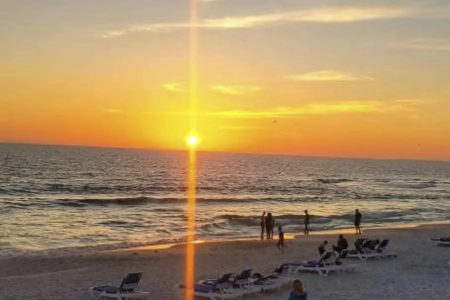 A sunset over the ocean, with beachgoers near the shoreline.