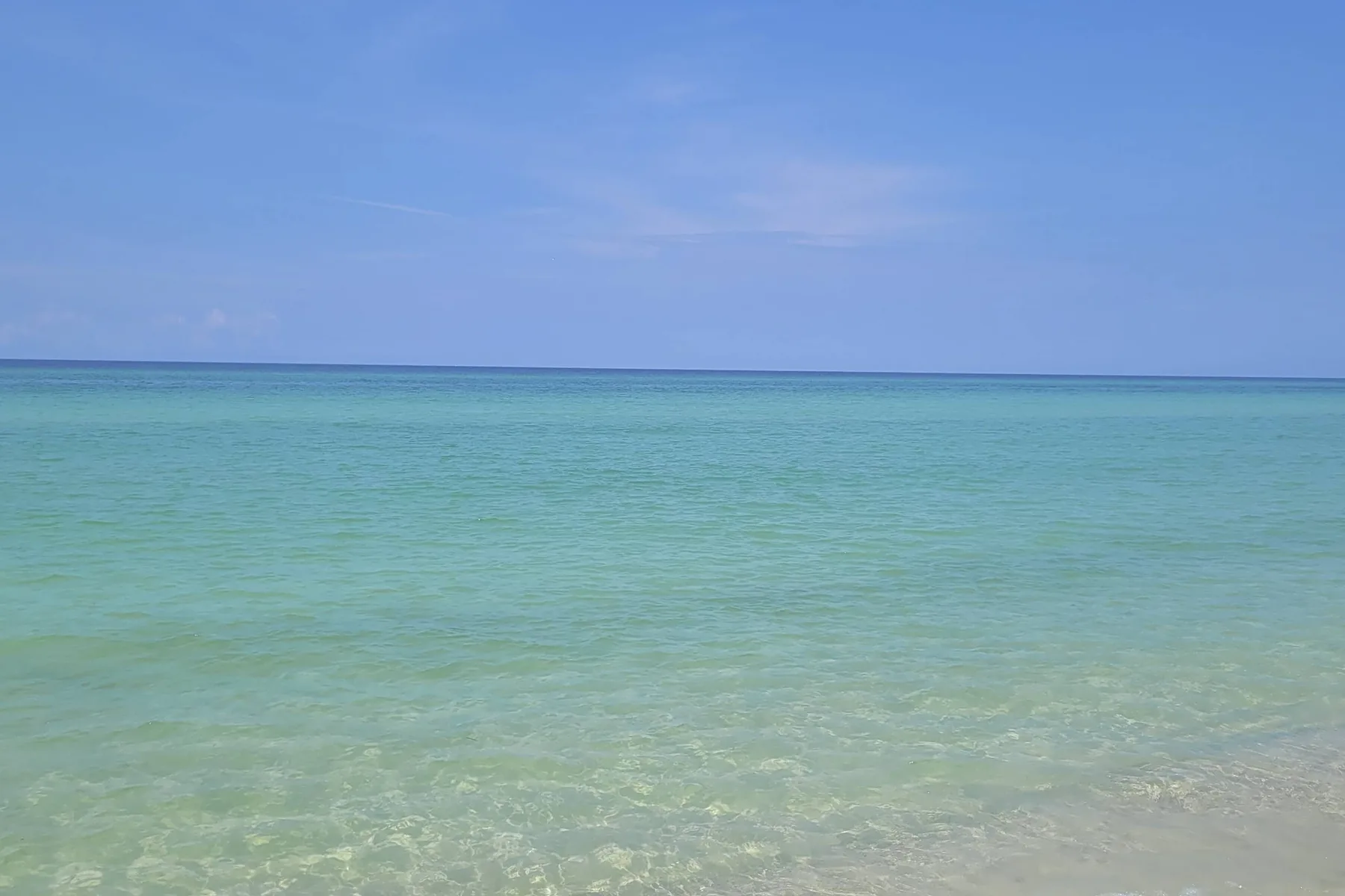 A calm beach scene with clear turquoise water beneath a blue sky.