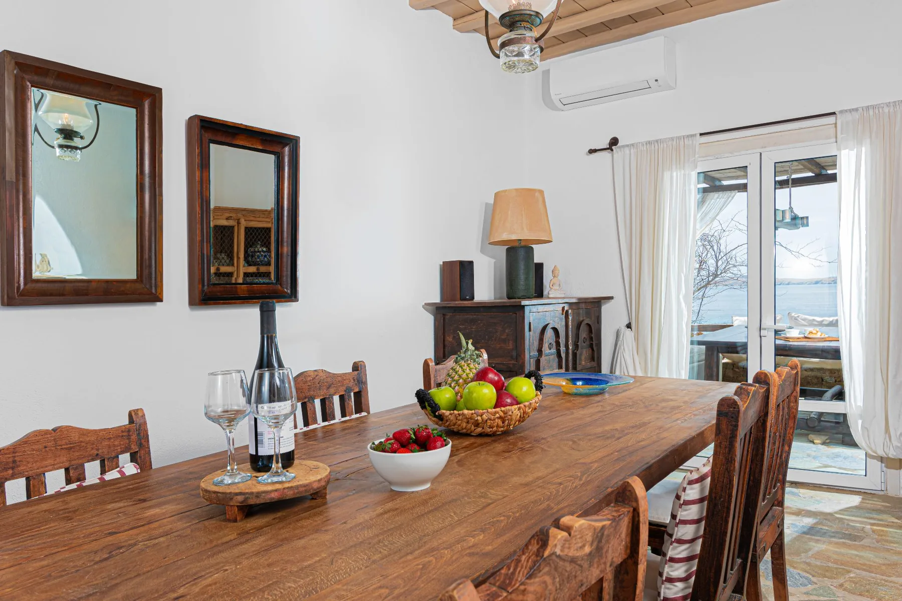 A dining room with a wooden table set with fruit and wine glasses.