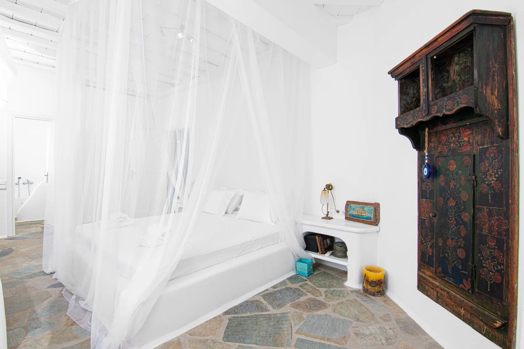 A bright bedroom with a white bed beneath sheer canopy curtains.