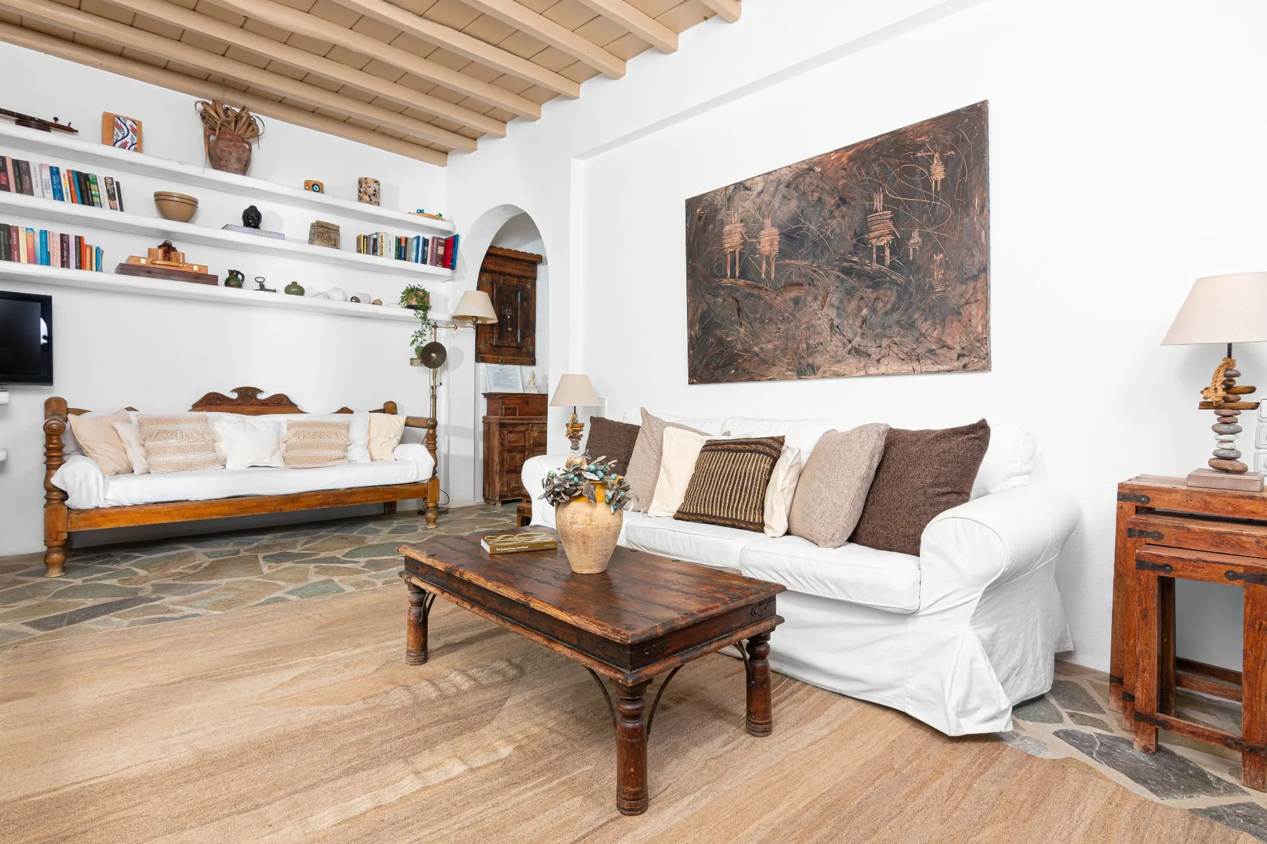 A living room with white seating, a wooden coffee table, and shelves along the wall.