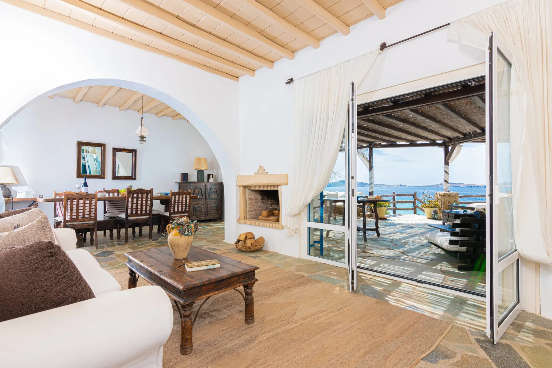 A bright living and dining area opens onto a covered terrace overlooking the sea.