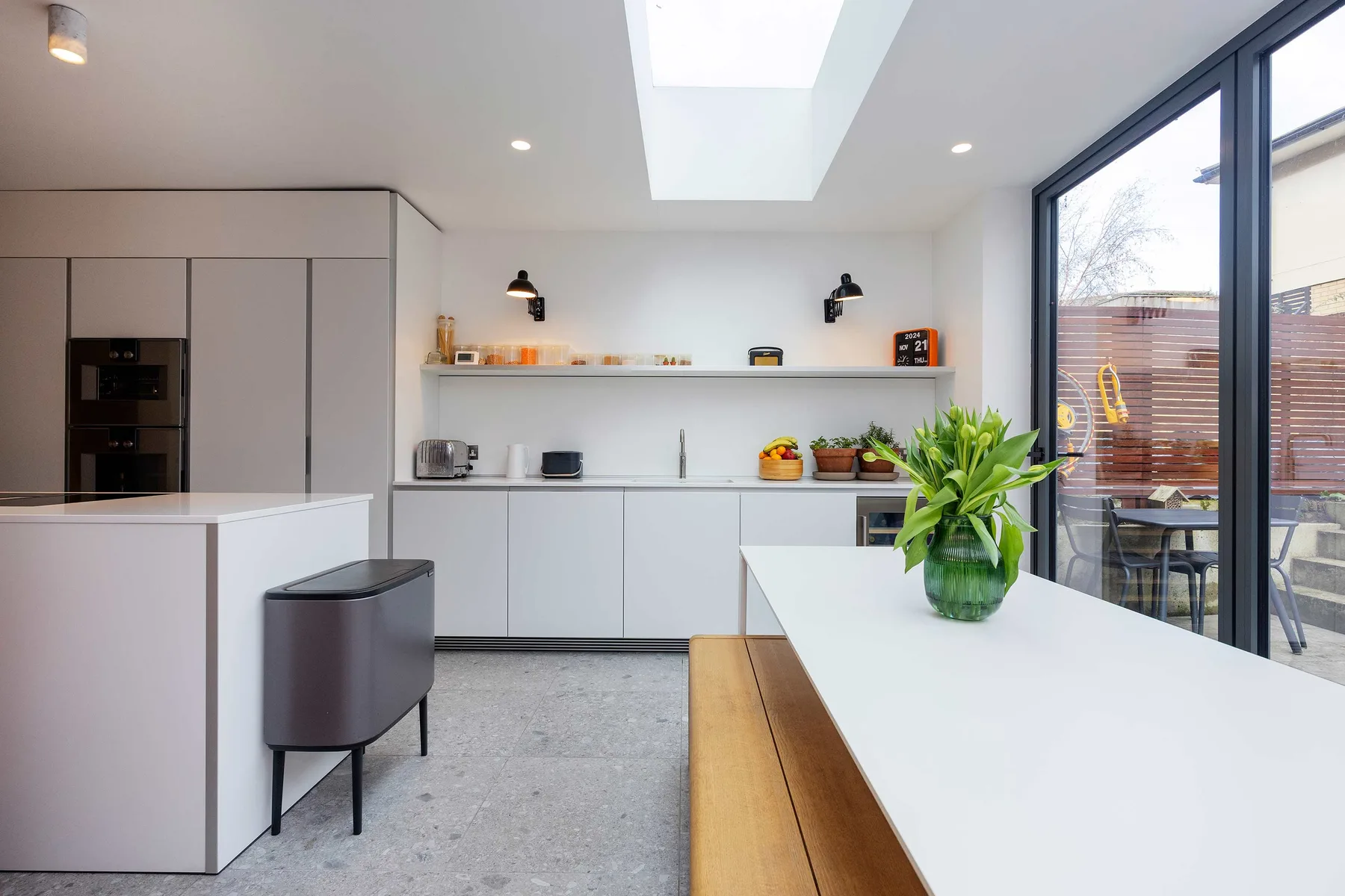 A bright modern kitchen with a long white island and large windows.