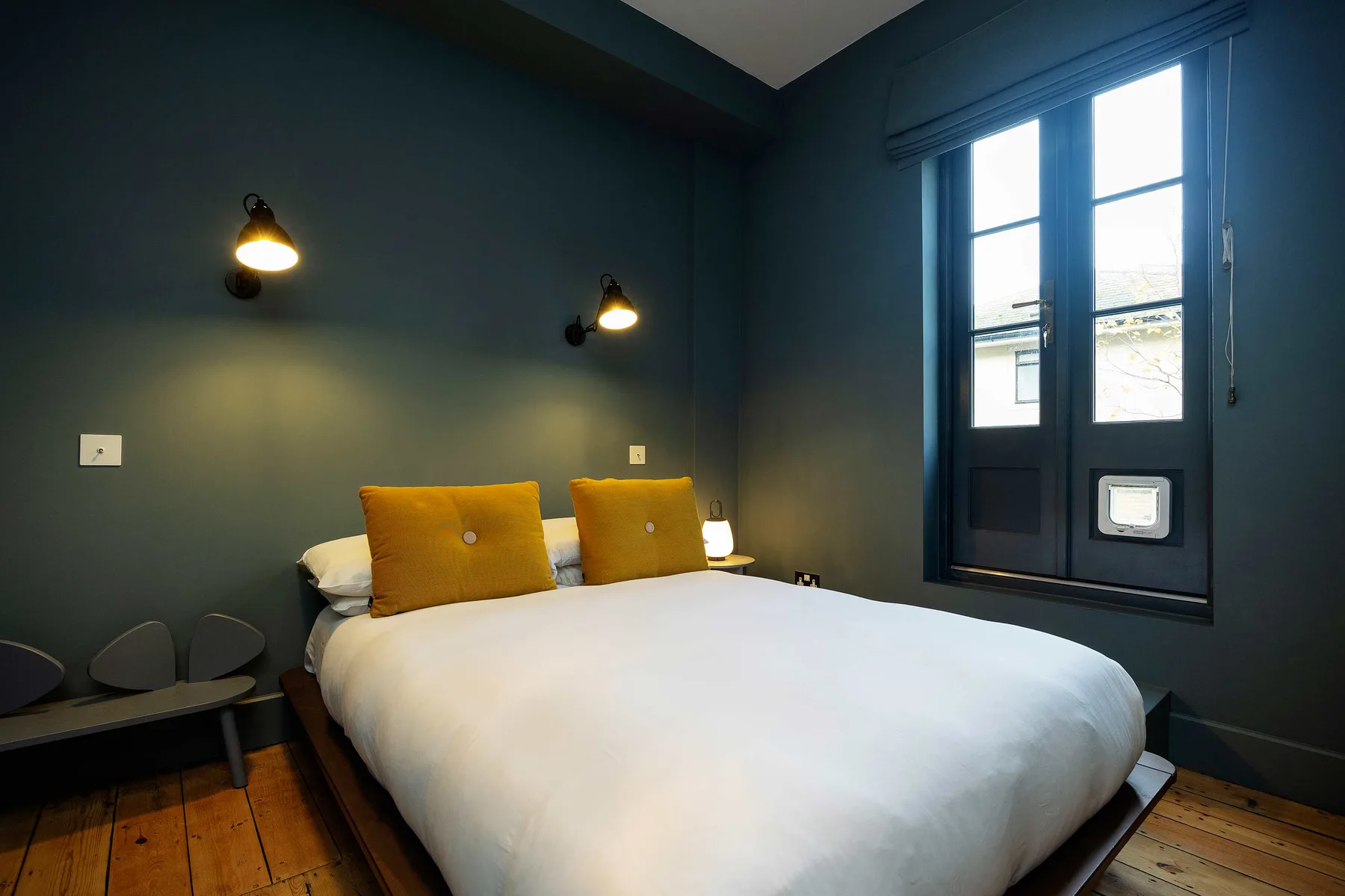 A bedroom with a bed beneath dark walls and beside a tall window.