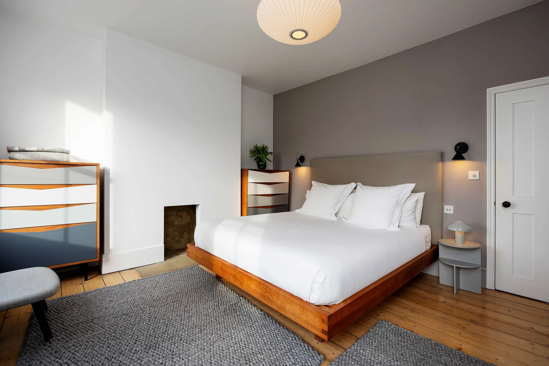 Dormitorio con una cama bien tendida, mesitas de noche y una alfombra gris.