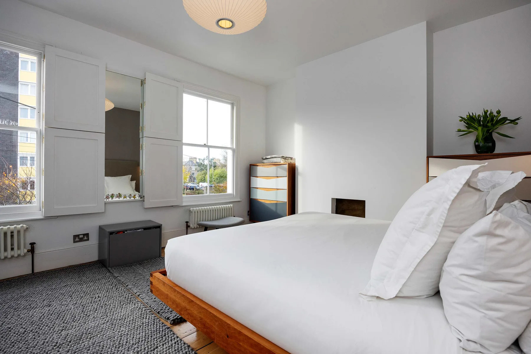 Un dormitorio luminoso con una cama grande, ventanas altas y una alfombra gris.