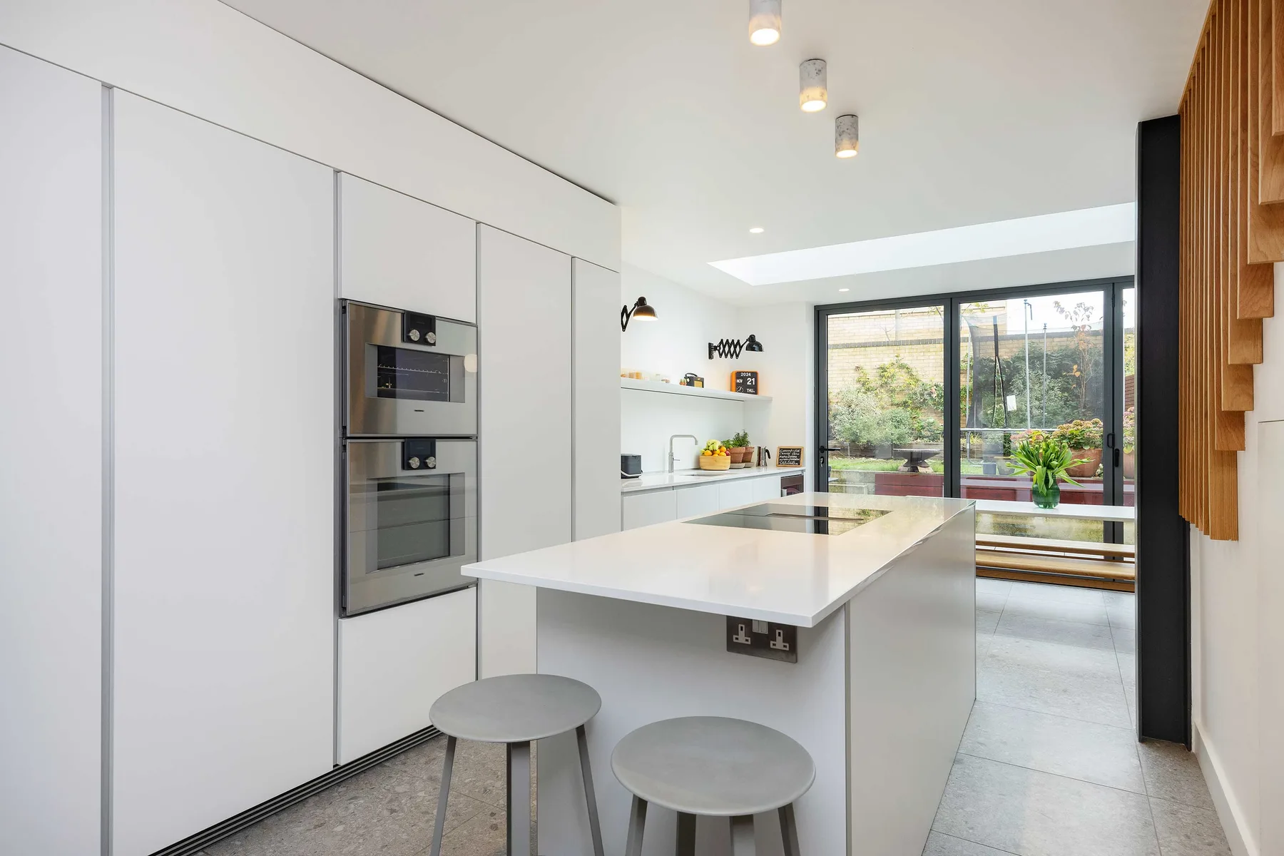 Una cocina moderna con una isla blanca y grandes ventanas con vista a la vegetación.