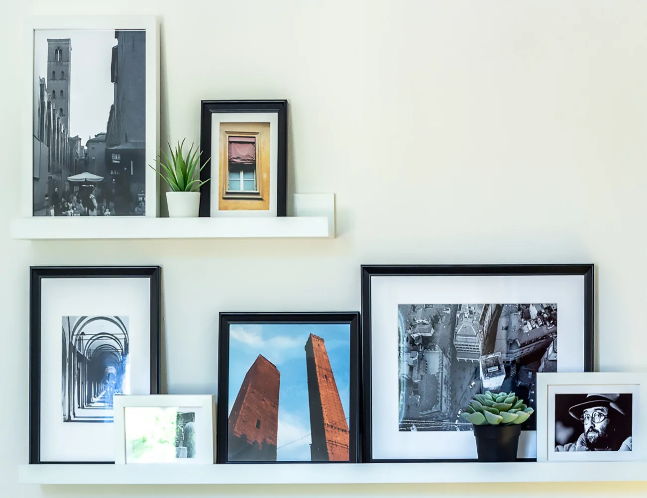 Framed photographs and artwork are displayed on white shelves against a light wall.