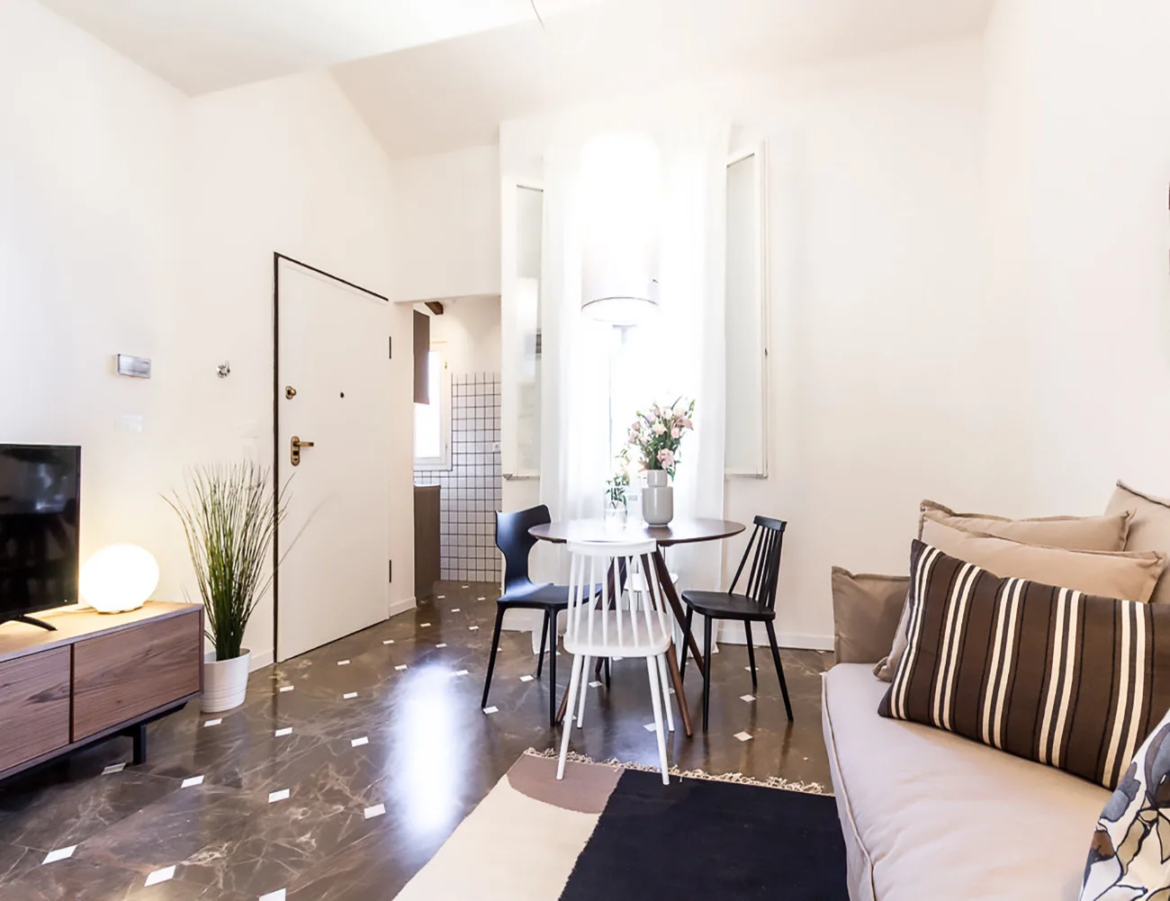 Una sala luminosa con mesa de comedor, asientos y una entrada abierta.
