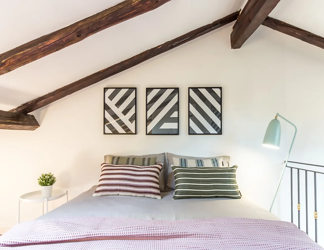 Un dormitorio con una cama, almohadas a rayas y cuadros geométricos en la pared.