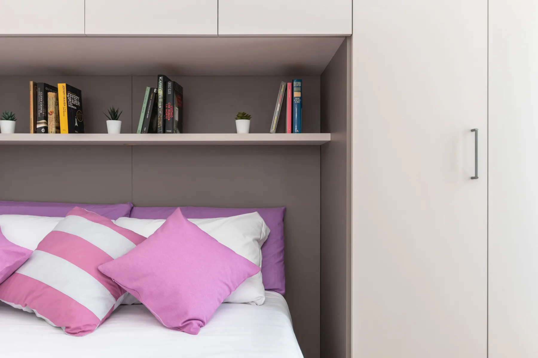 A bedroom with a bed beneath built-in shelving and cabinets.