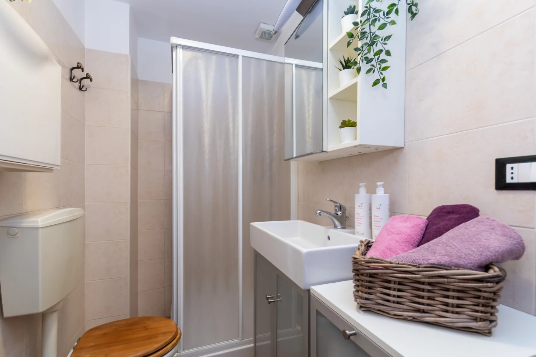 A bathroom with a sink, shower, and towels in a basket.