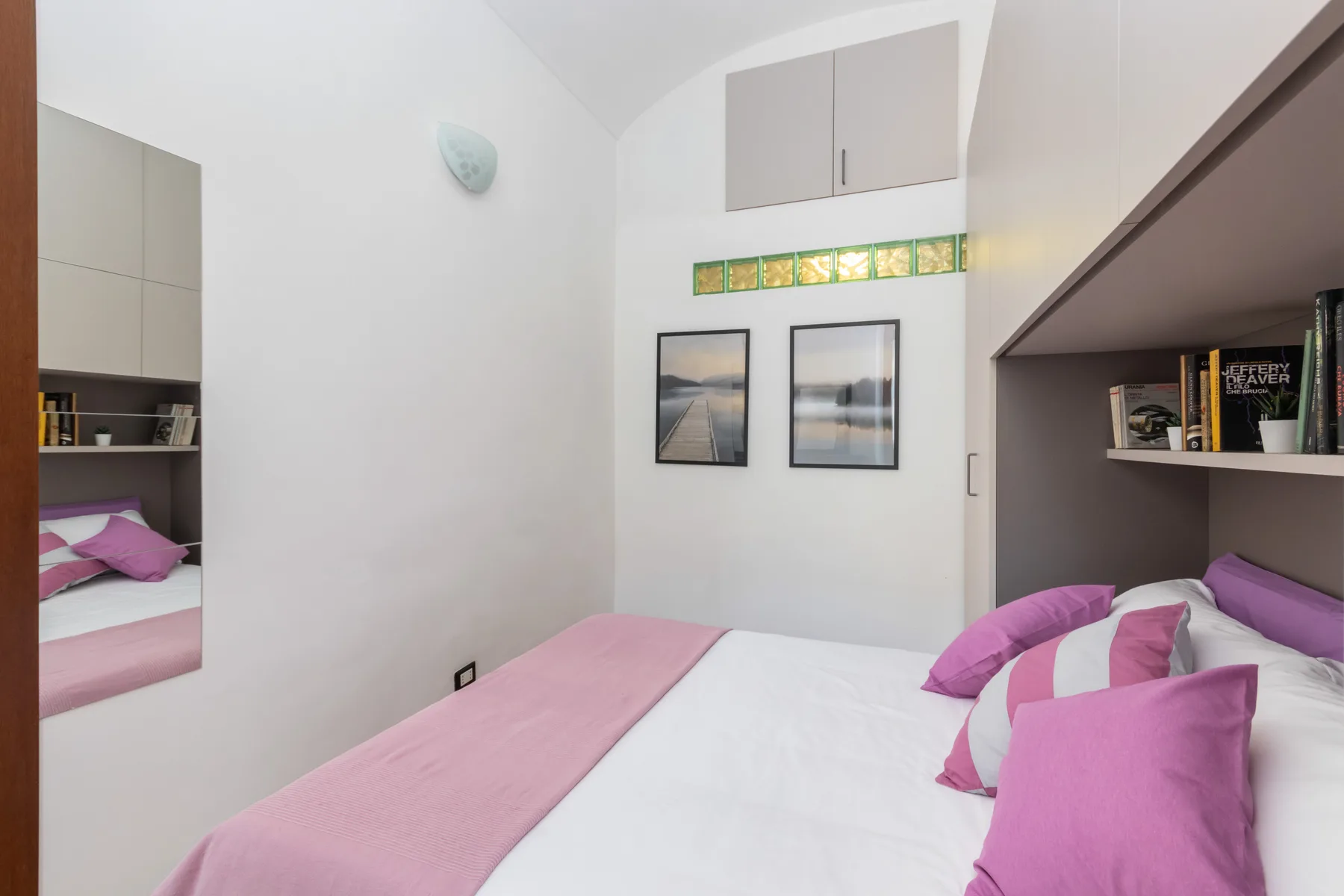 A bedroom with a bed dressed in pink and white linens and framed wall art.