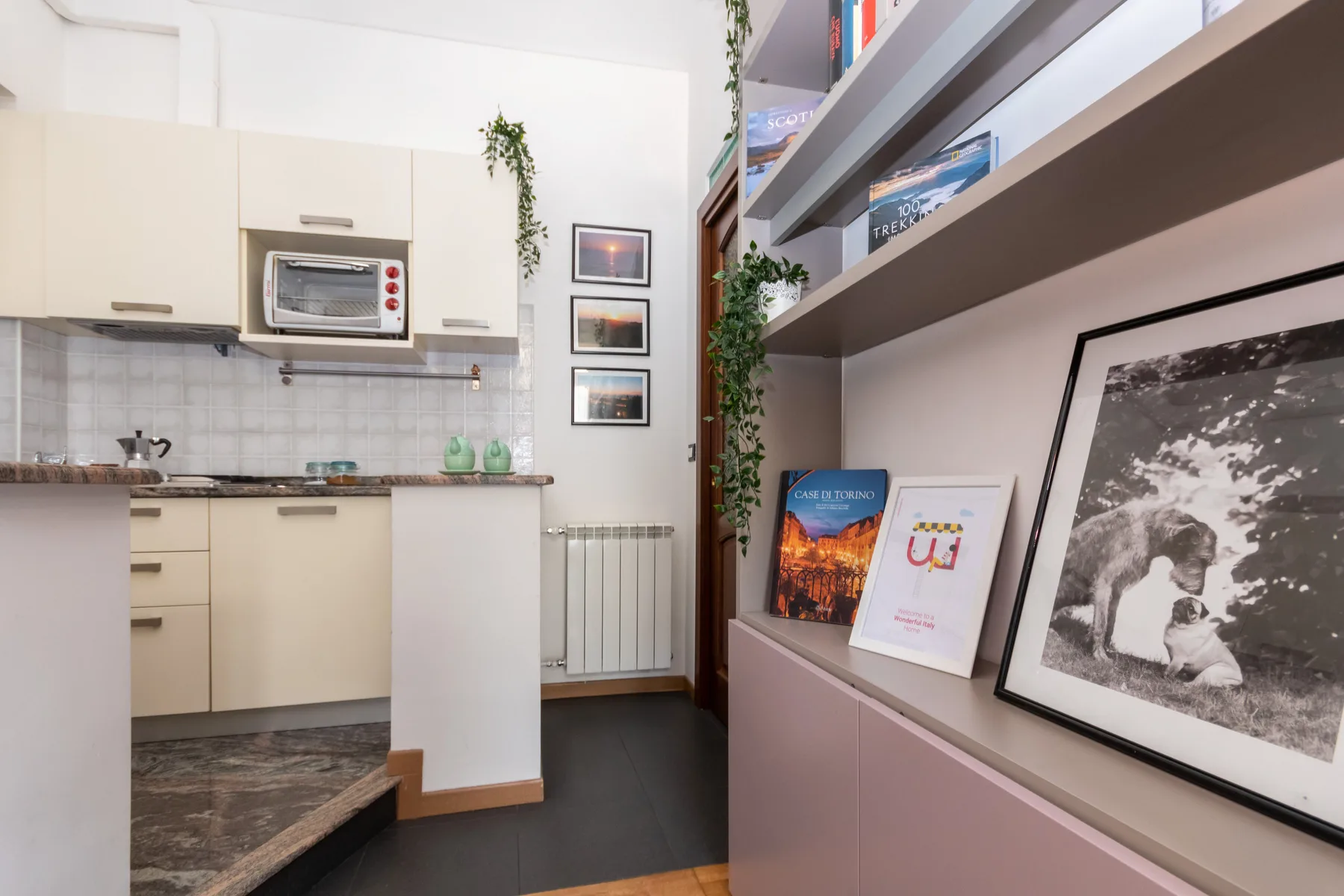 A compact kitchen beside built-in shelving displaying books and framed artwork.