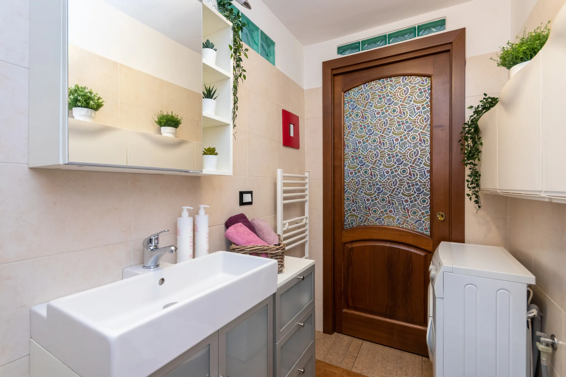 A bright bathroom with a sink, wooden door, and washing machine.