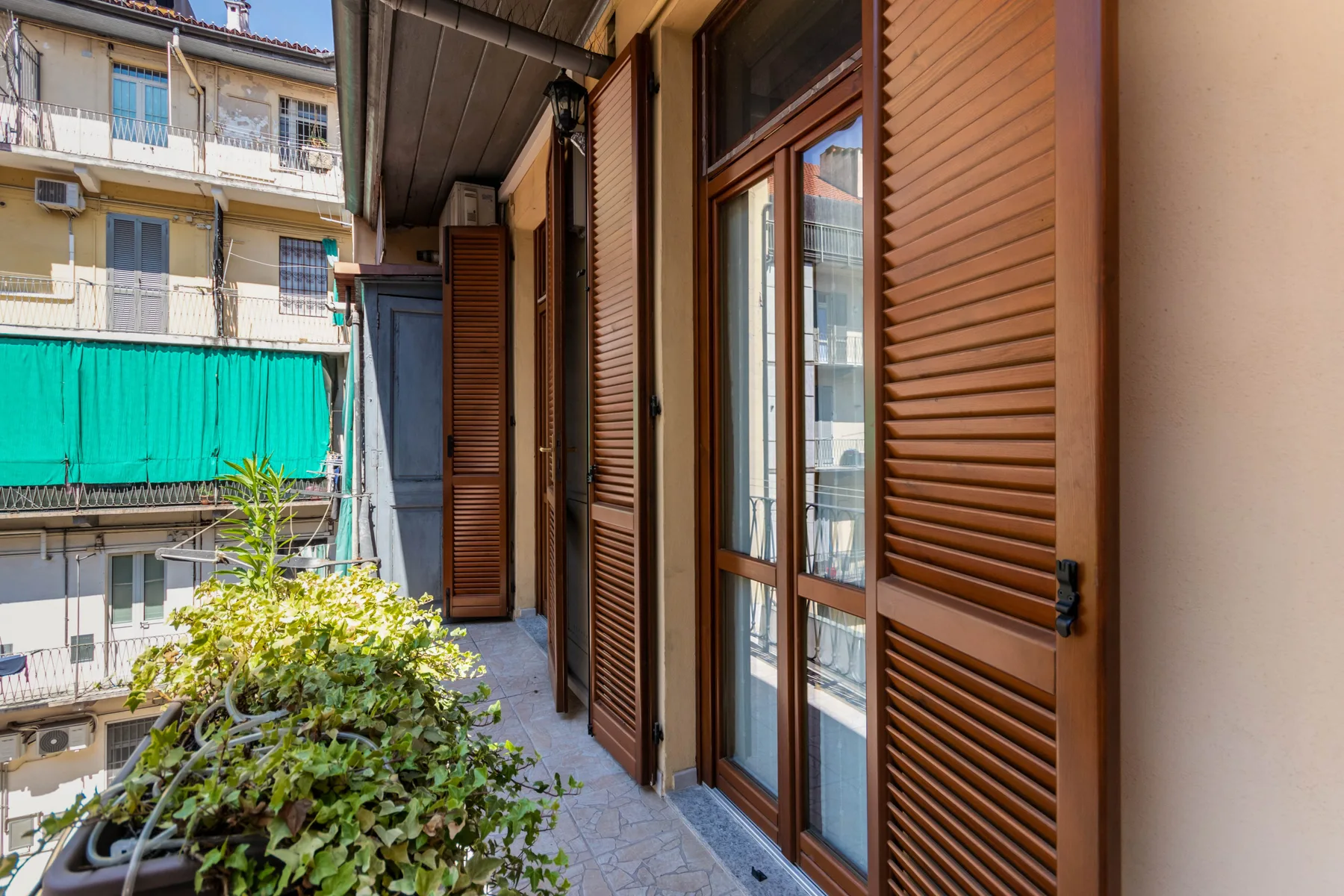 A narrow balcony walkway runs alongside brown shutters and glass doors.