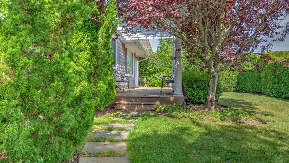 A garden path leads to a small covered patio among trees and hedges.