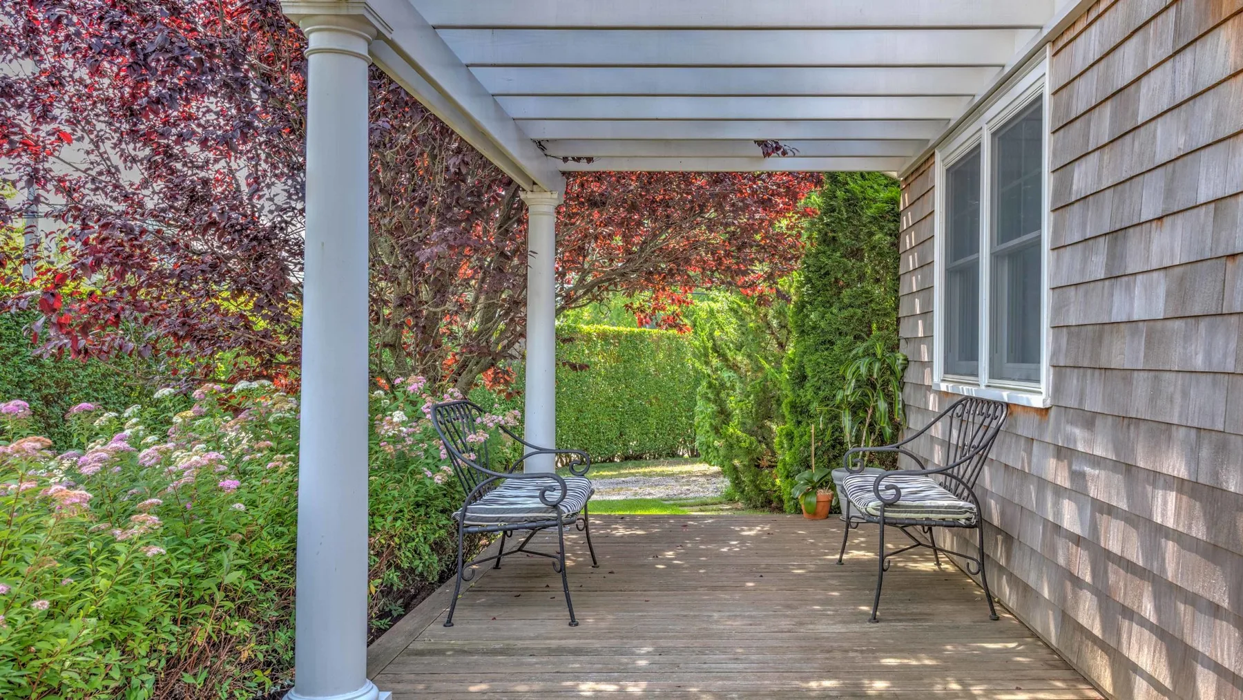 A covered outdoor porch with seating overlooks a garden.