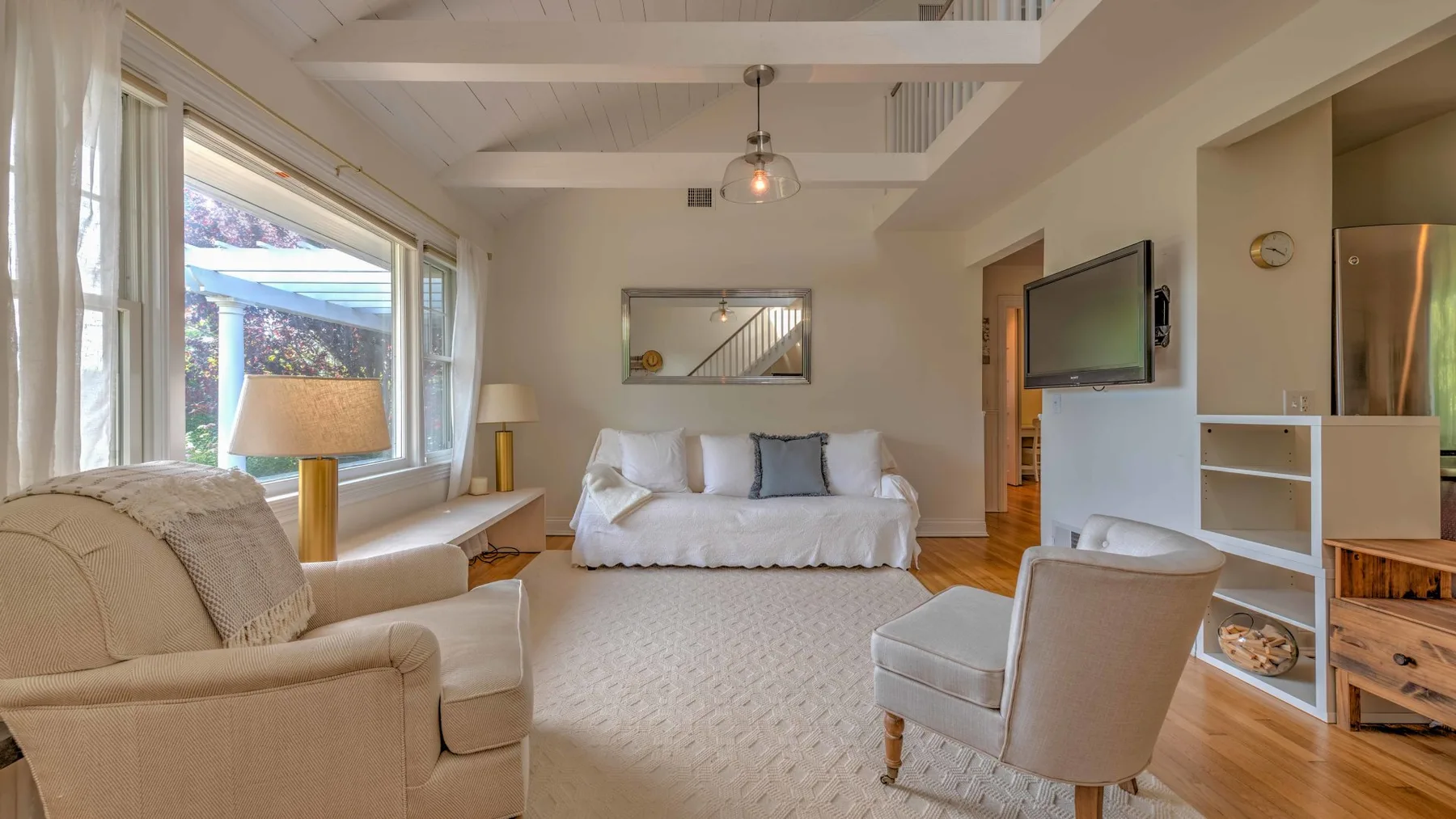 A bright living room with seating arranged around a central rug and a wall-mounted television.