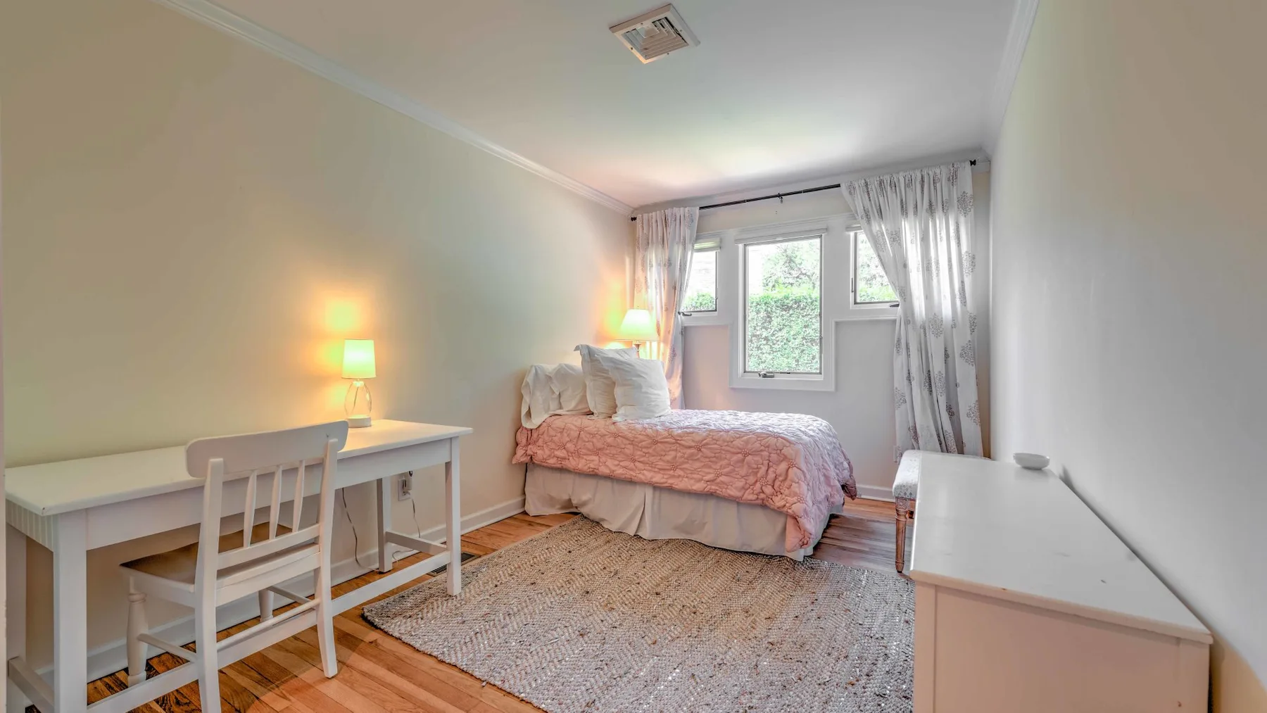 A bedroom with a bed, desk, and large window.