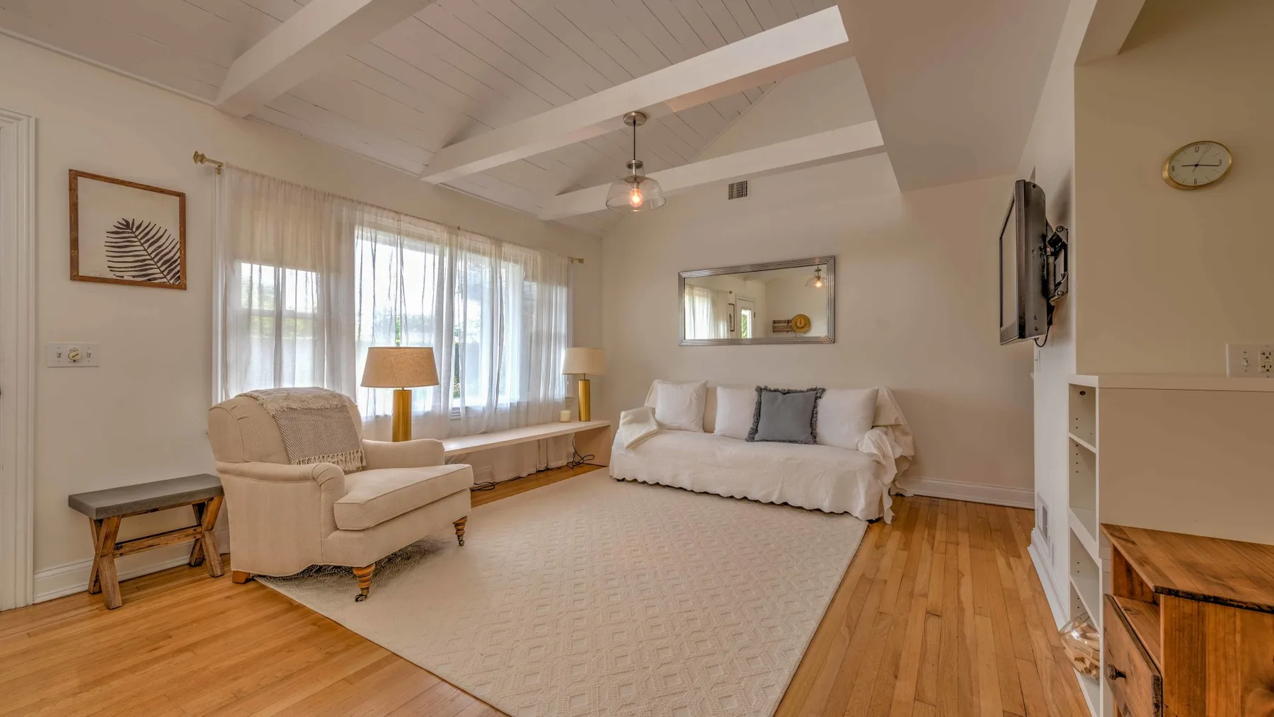 A bright living room with seating beside large windows and a bed against the far wall.