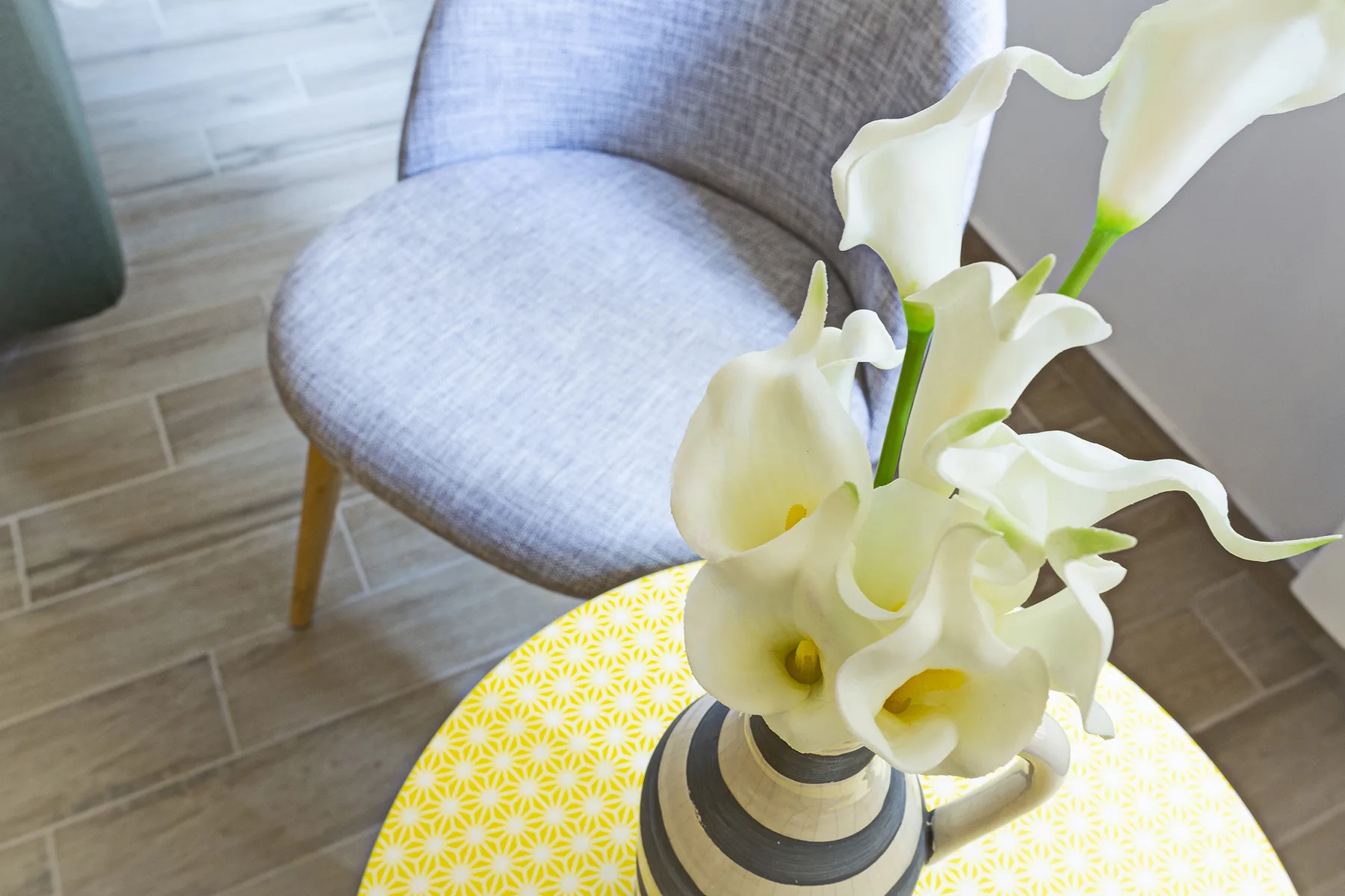 A vase of white flowers sits on a patterned table beside a chair.