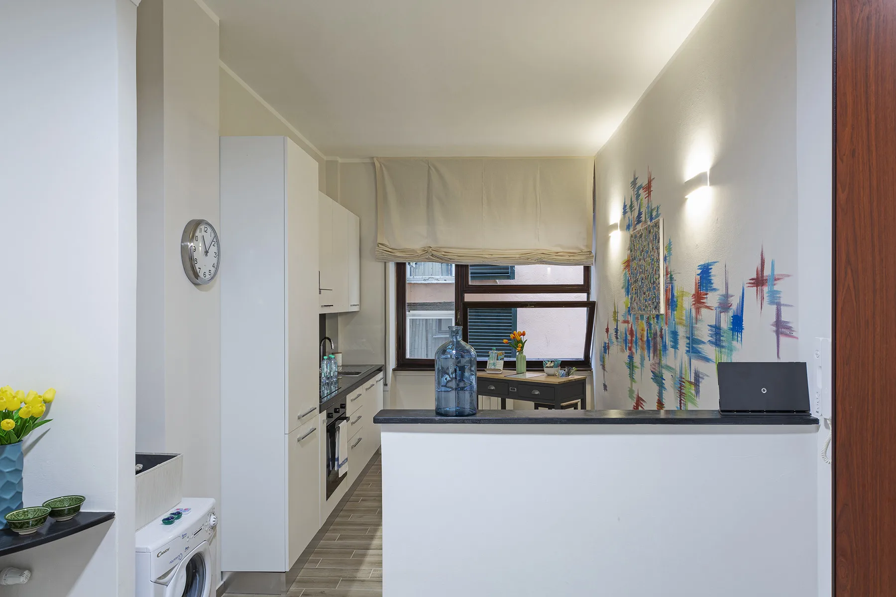 A compact kitchen opens onto a small dining area, with colorful wall art.