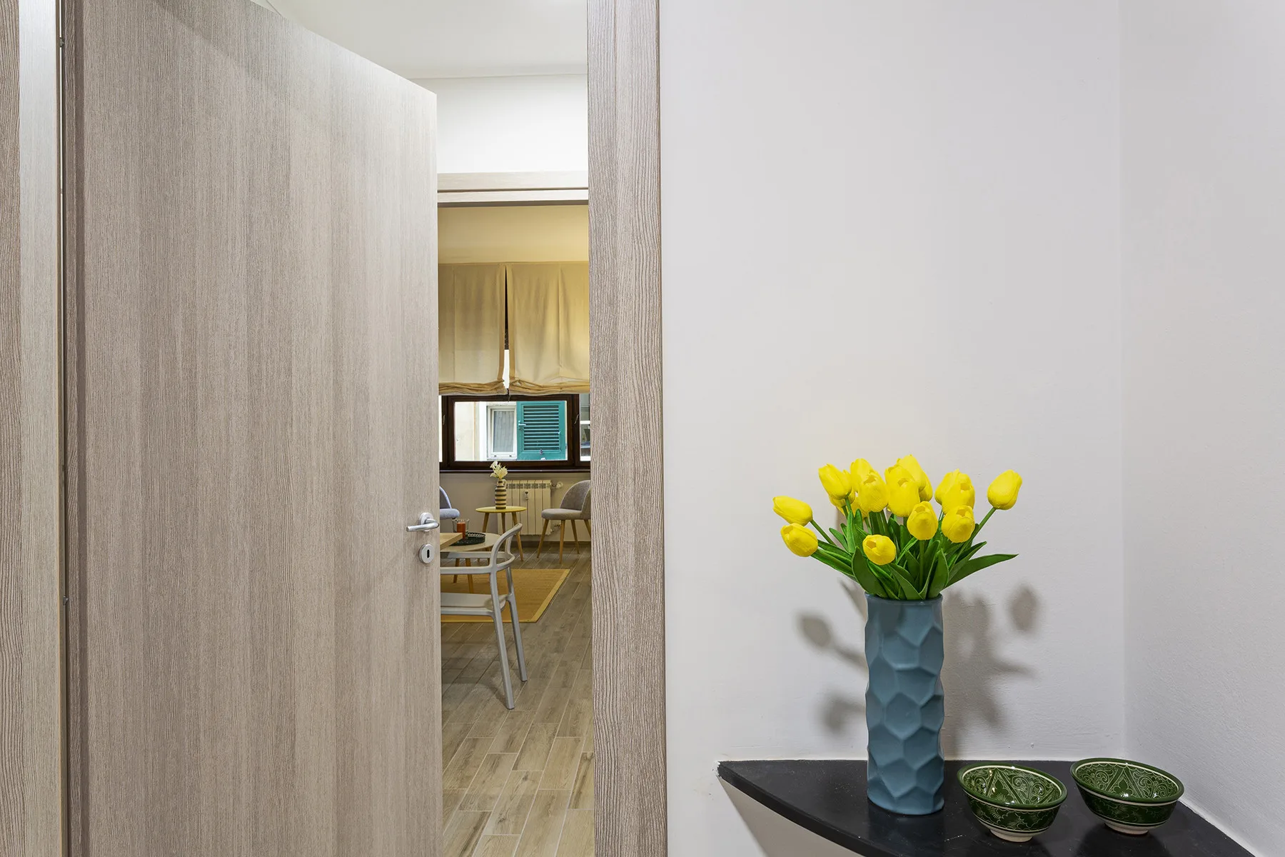 An open doorway reveals a dining area with a vase of yellow flowers nearby.