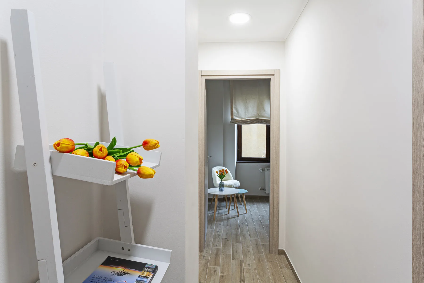 A bright hallway leads to a small room with a chair and table.