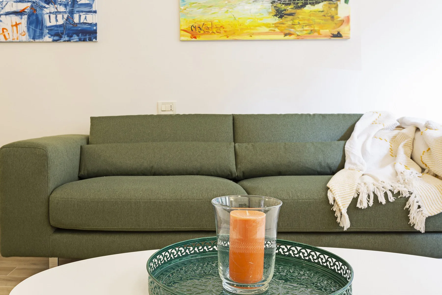 A green sofa sits against a pale wall, with a candle on the table in front.