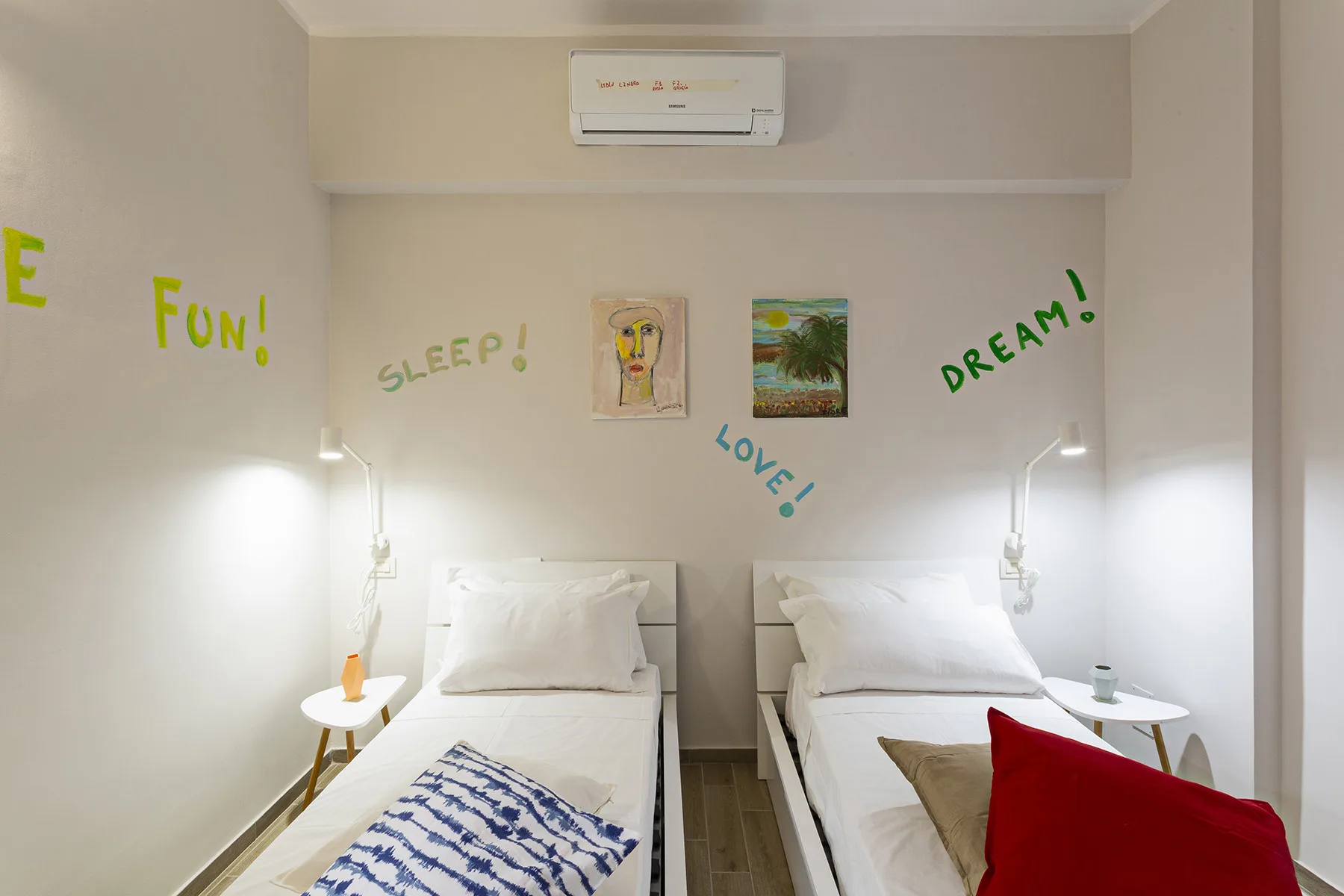 A bedroom with two beds, wall art, and an air conditioner.