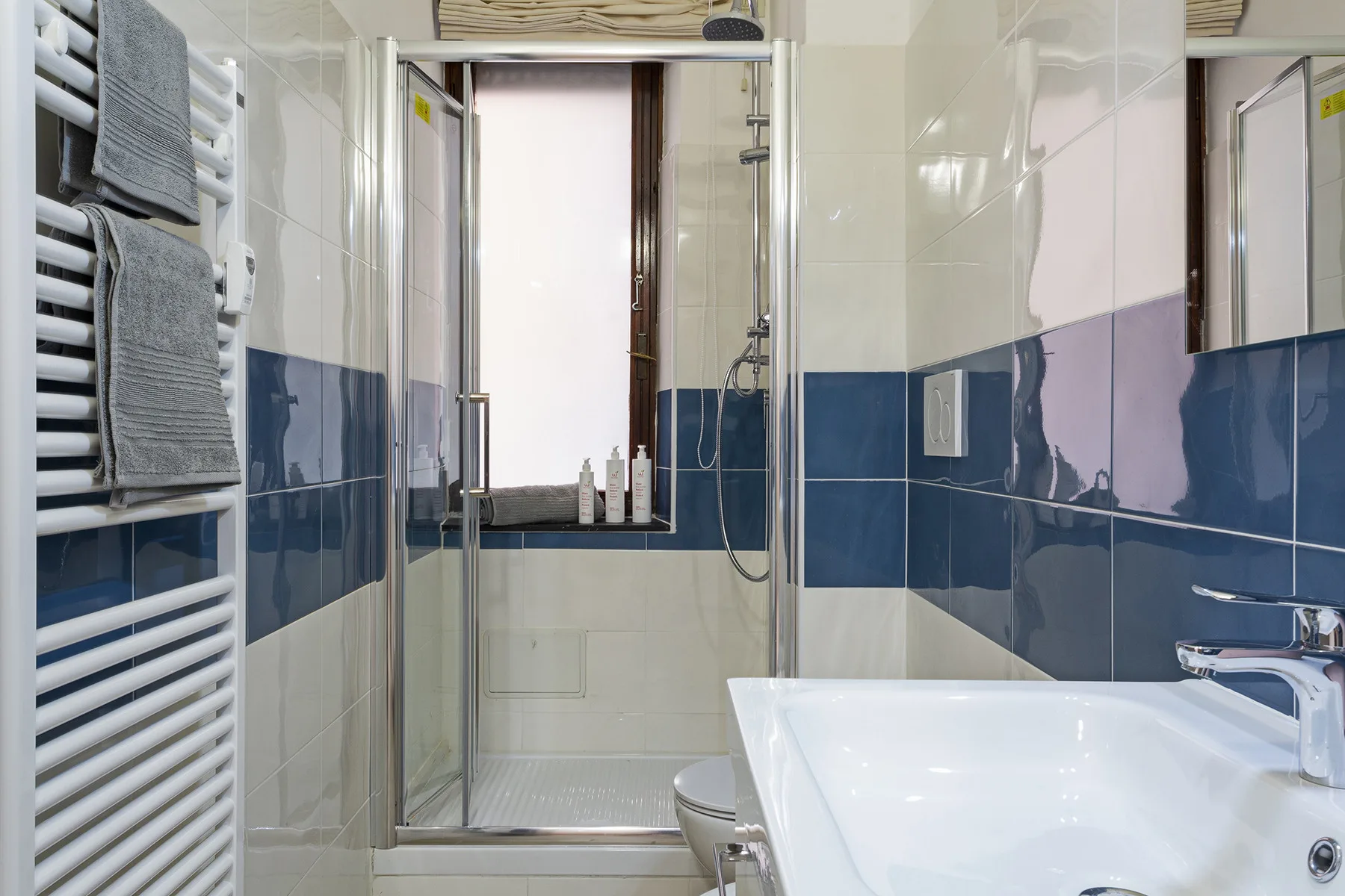 A bathroom with a glass shower, bathtub, and towels on a heated rail.