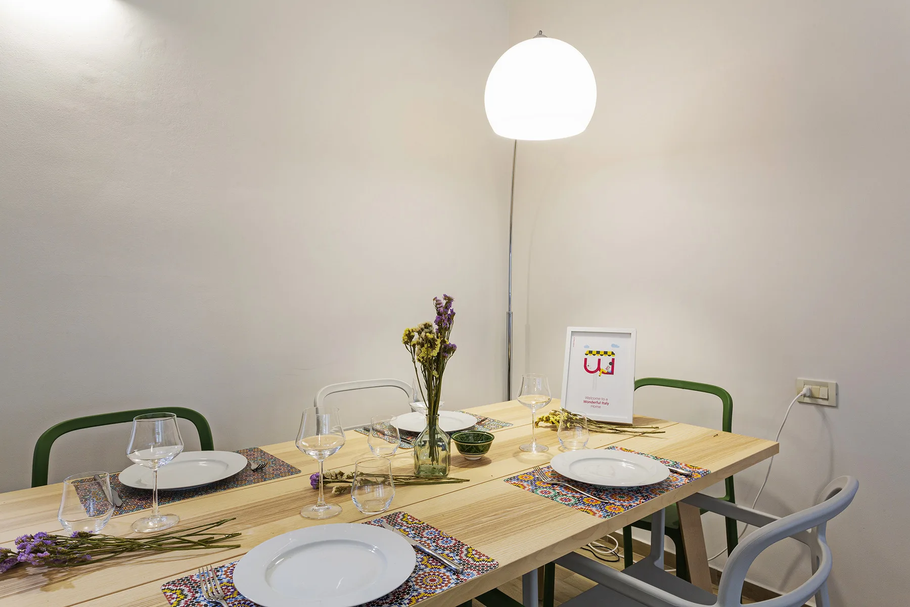 A dining table is set with plates and glasses beneath a hanging lamp.