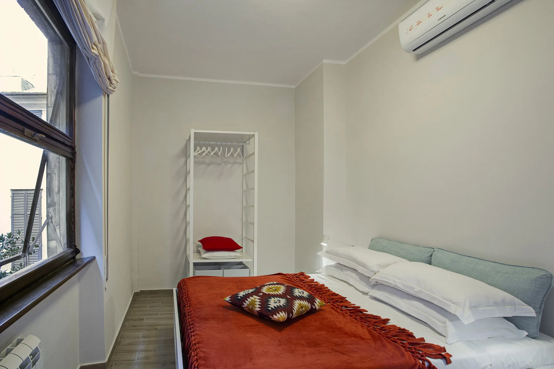 A bedroom with a bed covered by a red blanket beside a large window.