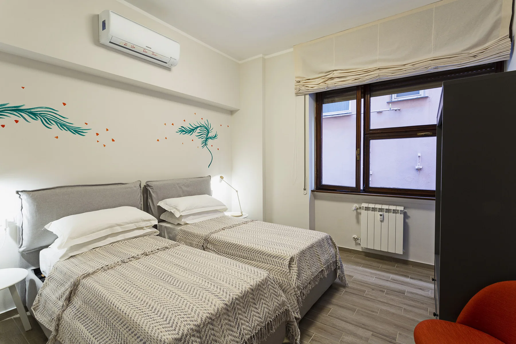 A bedroom with two single beds and a window overlooking a neighboring building.