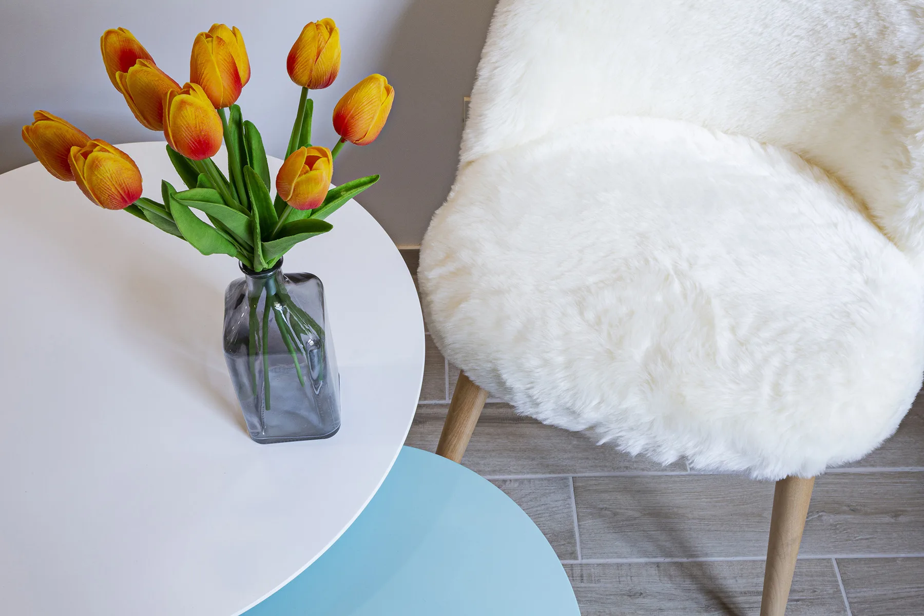 A white seating area beside a round table with a vase of tulips.