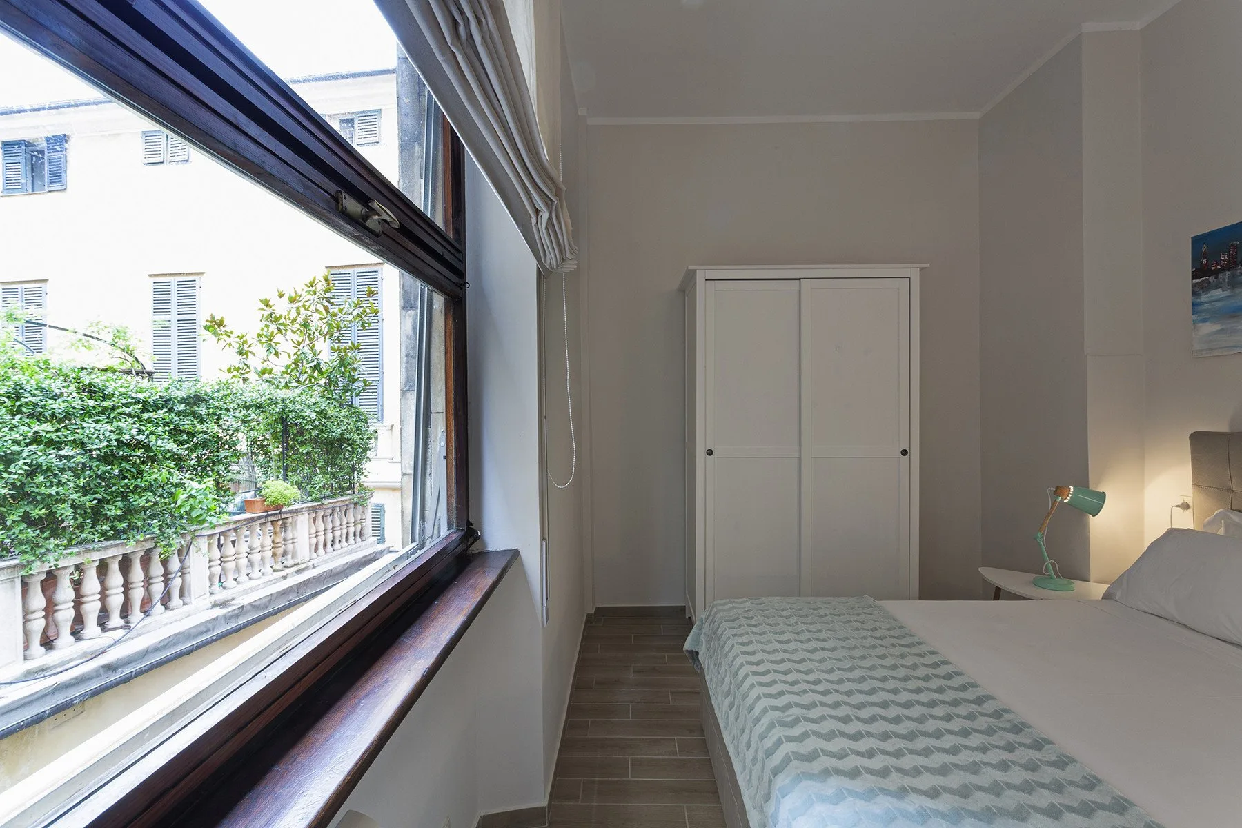 A bedroom with a bed beside a large window overlooking greenery.