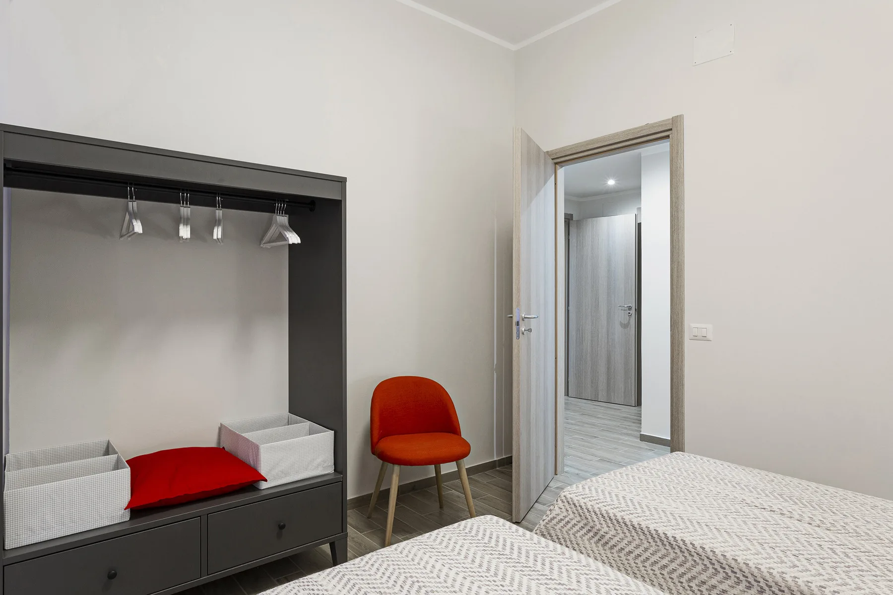 A bedroom with a bed, an open wardrobe, and a red chair.