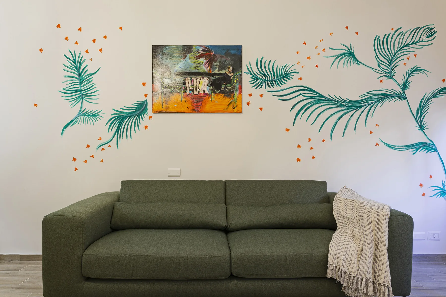 A living room with a dark sofa beneath colorful wall art and painted foliage.