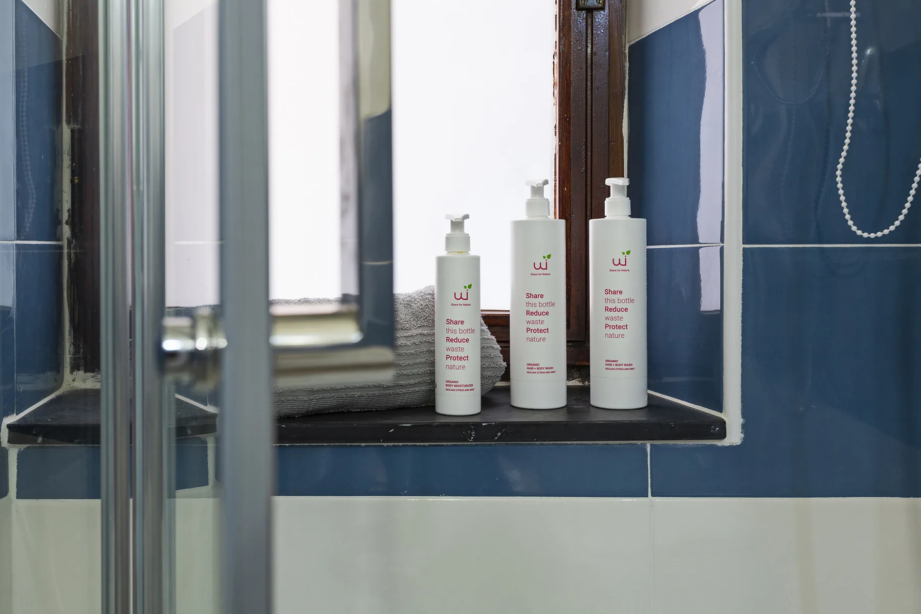 A bathroom shower area with blue tiled walls and bottles on a window ledge.