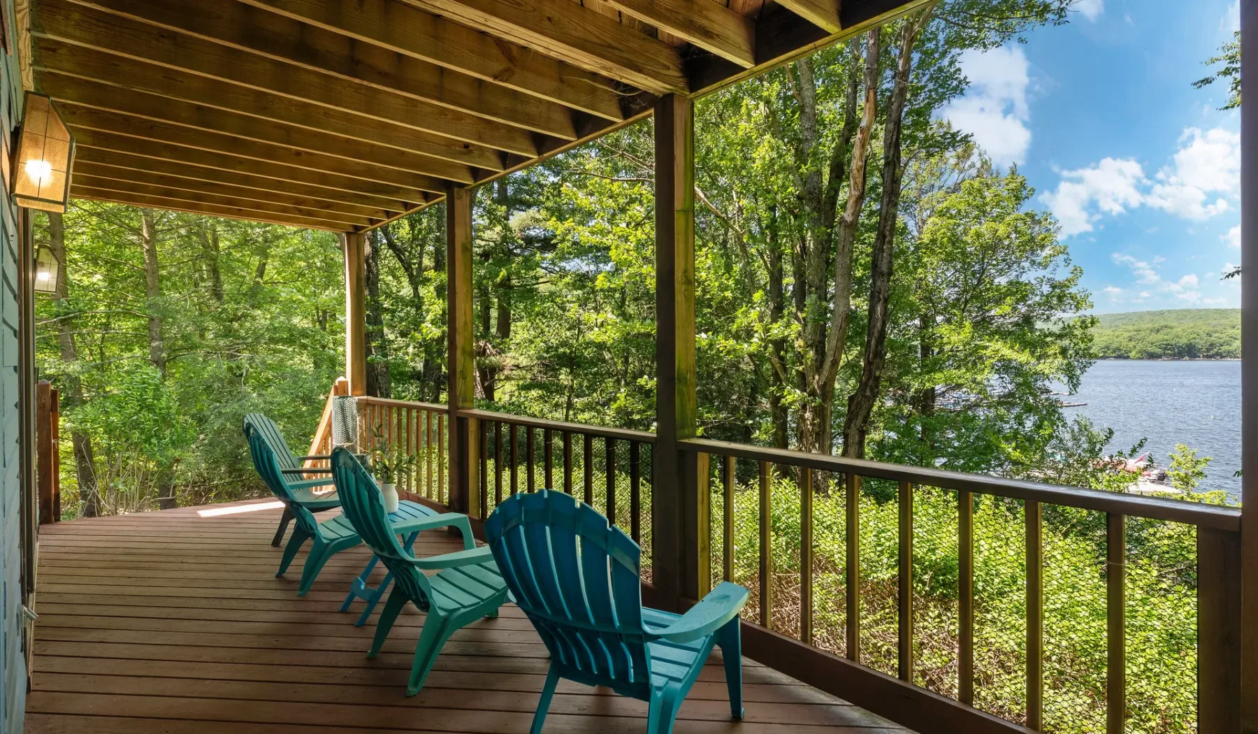 Una terraza de madera cubierta con asientos tiene vistas a un lago entre los árboles.