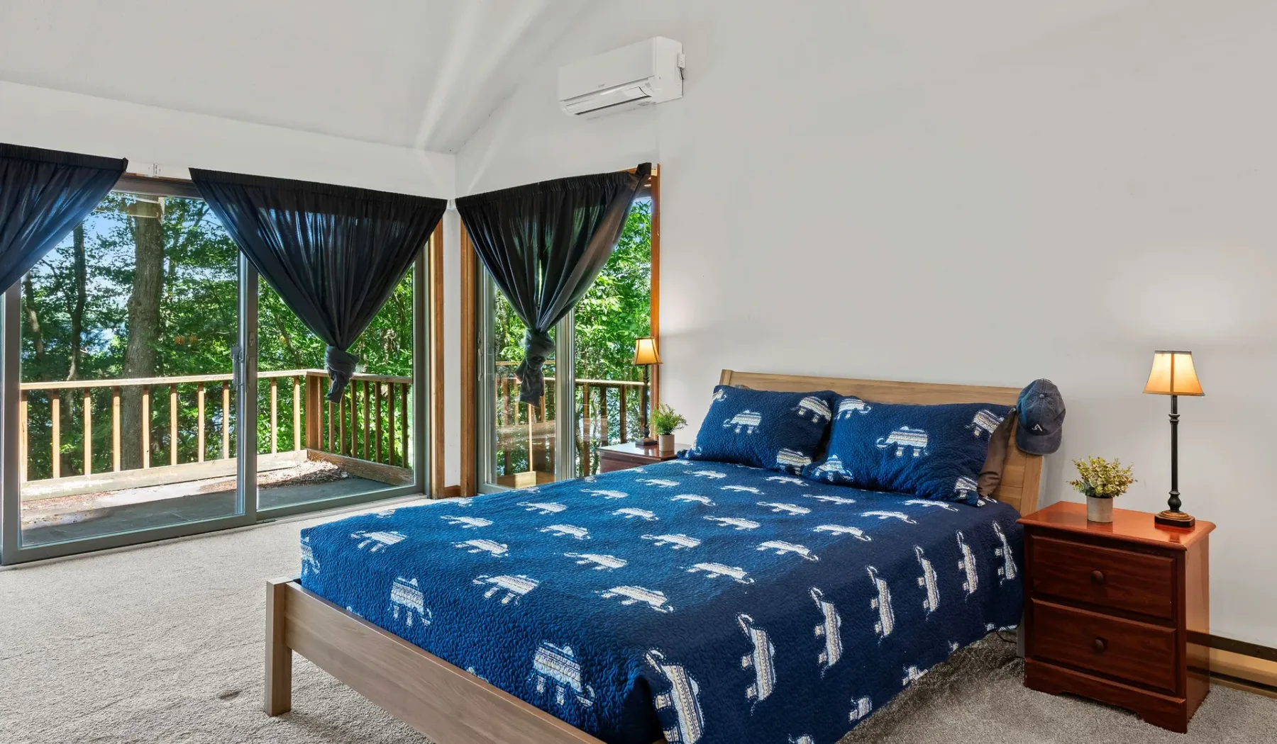 Un dormitorio con una colcha azul junto a grandes ventanas con cortinas.