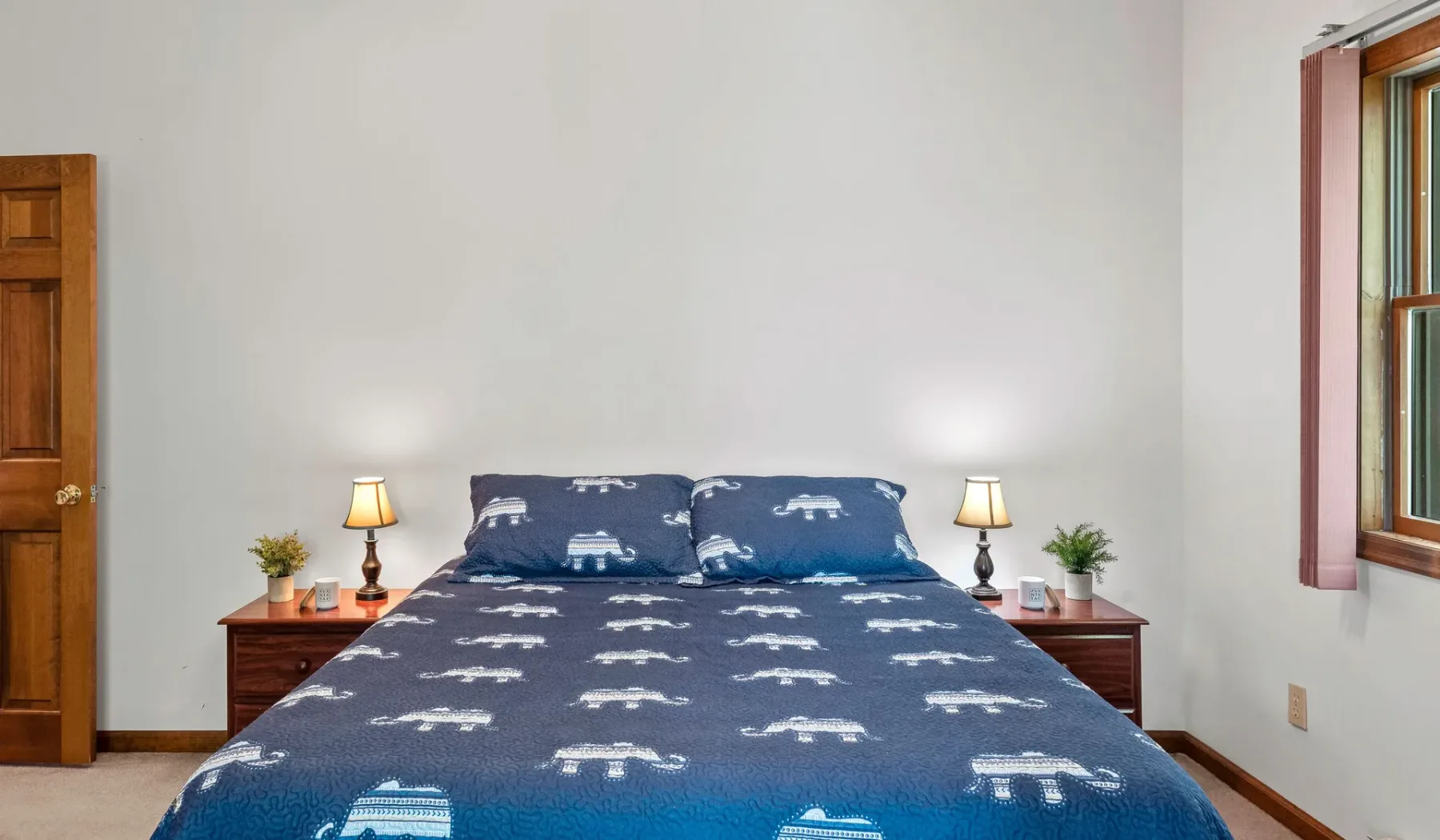 Un dormitorio con una cama vestida con ropa de cama azul estampada y mesas de noche.