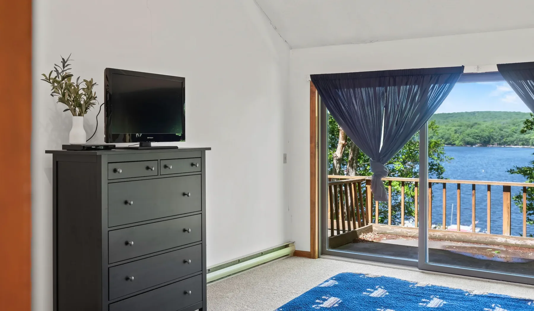 Un dormitorio da a un balcón con vistas al agua, con una cómoda junto a la puerta corrediza.